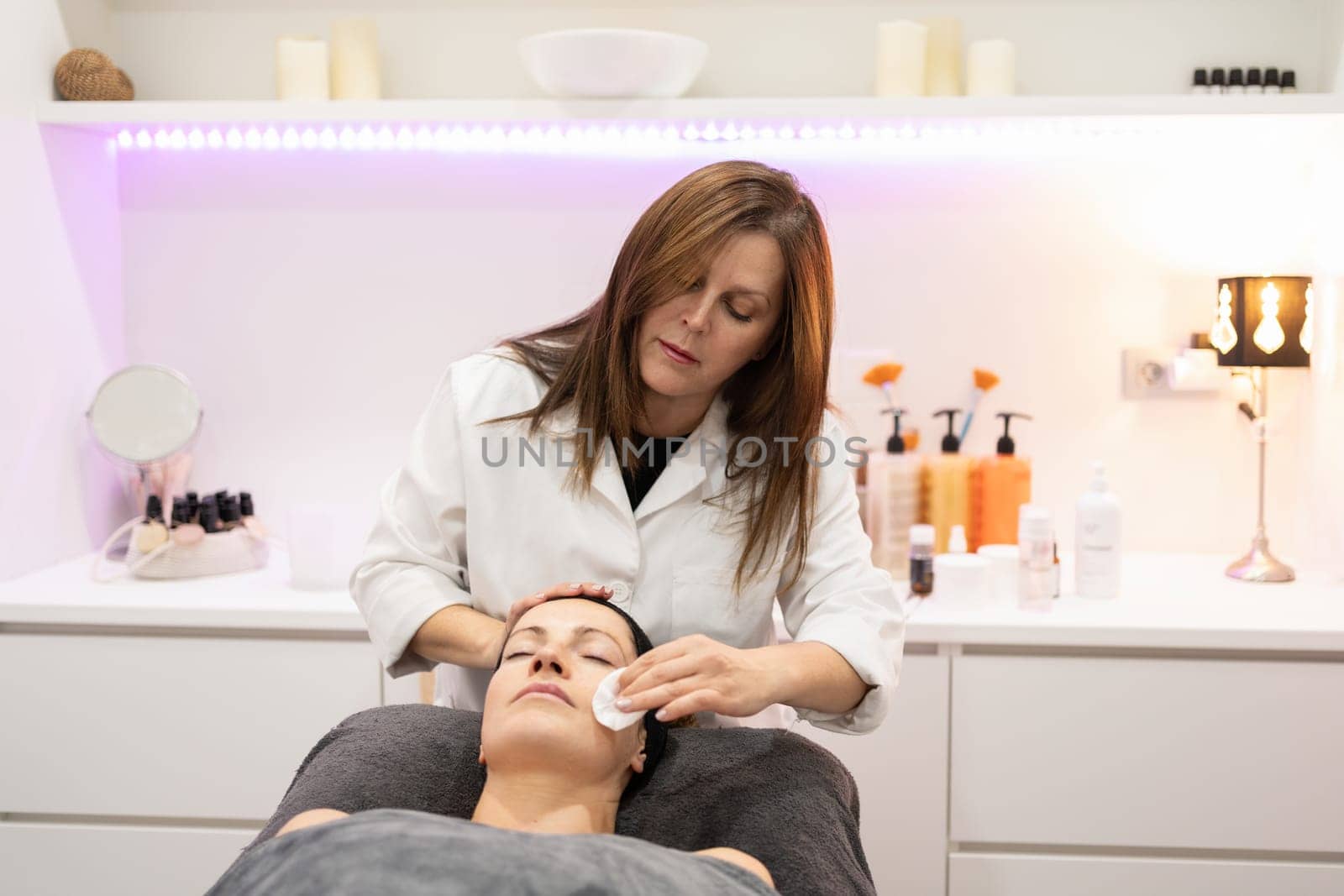 Beautician cleaning face of woman with cotton pad in beauty salon by javiindy