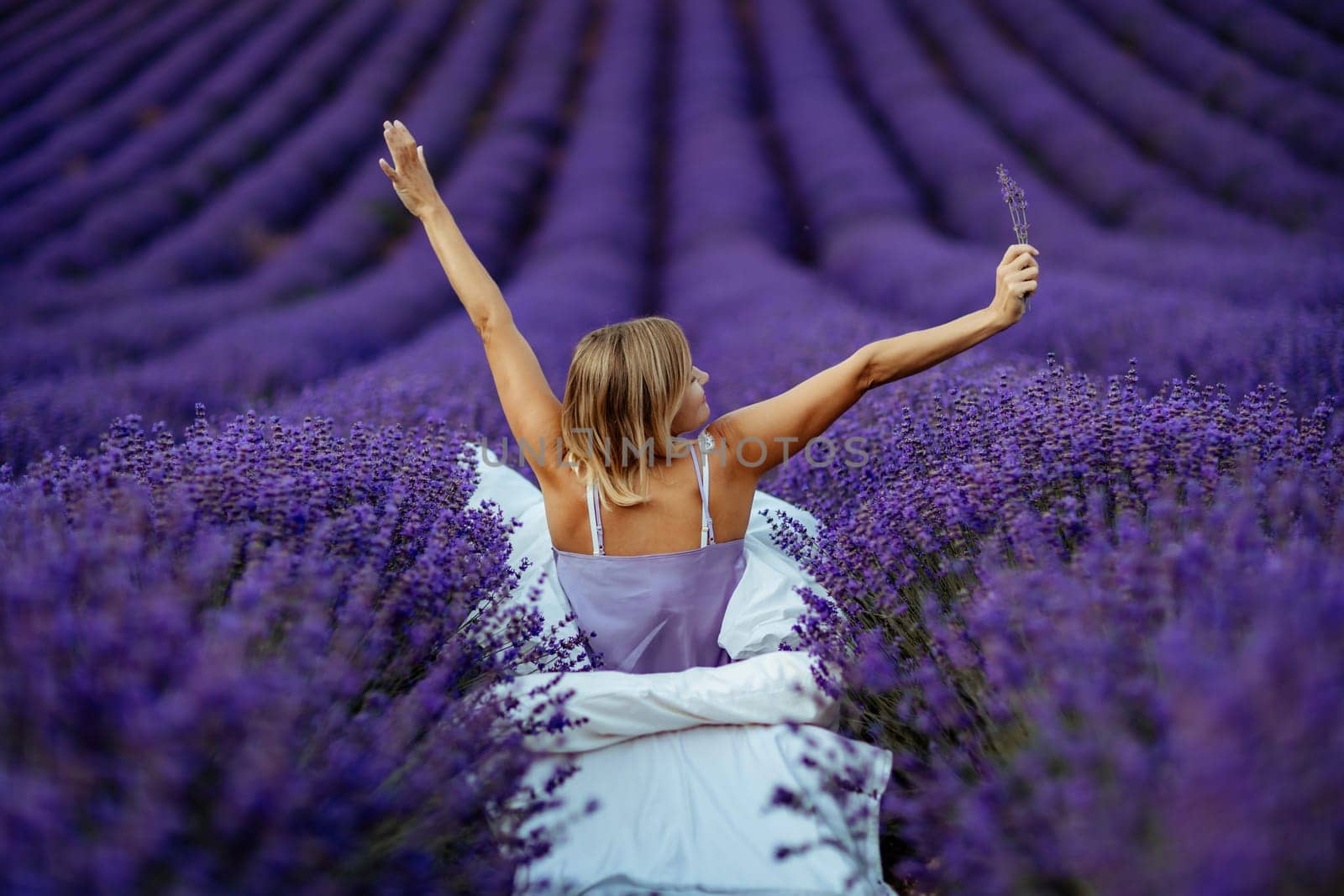 A middle-aged woman sits in a lavender field and enjoys aromatherapy. Aromatherapy concept, lavender oil, photo session in lavender.