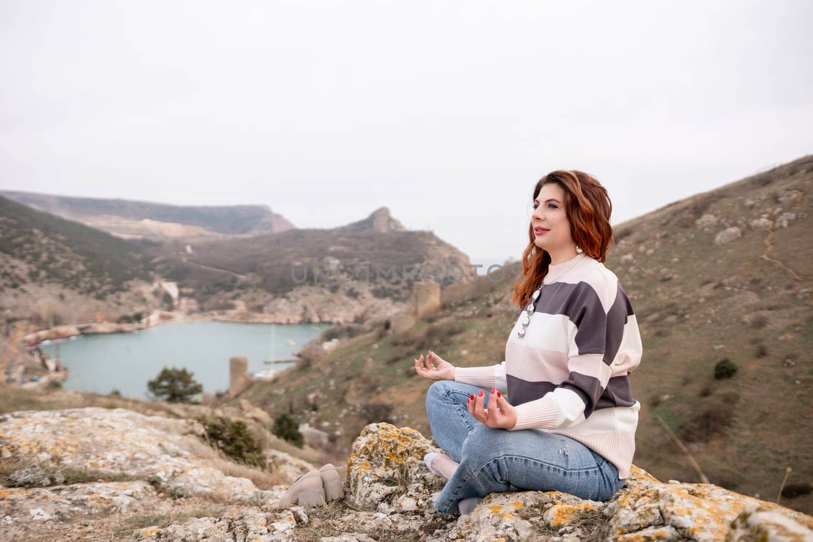 A woman is sitting on a rock overlooking a body of water. The scene is peaceful and serene, with the woman looking out over the water and taking in the view. by Matiunina