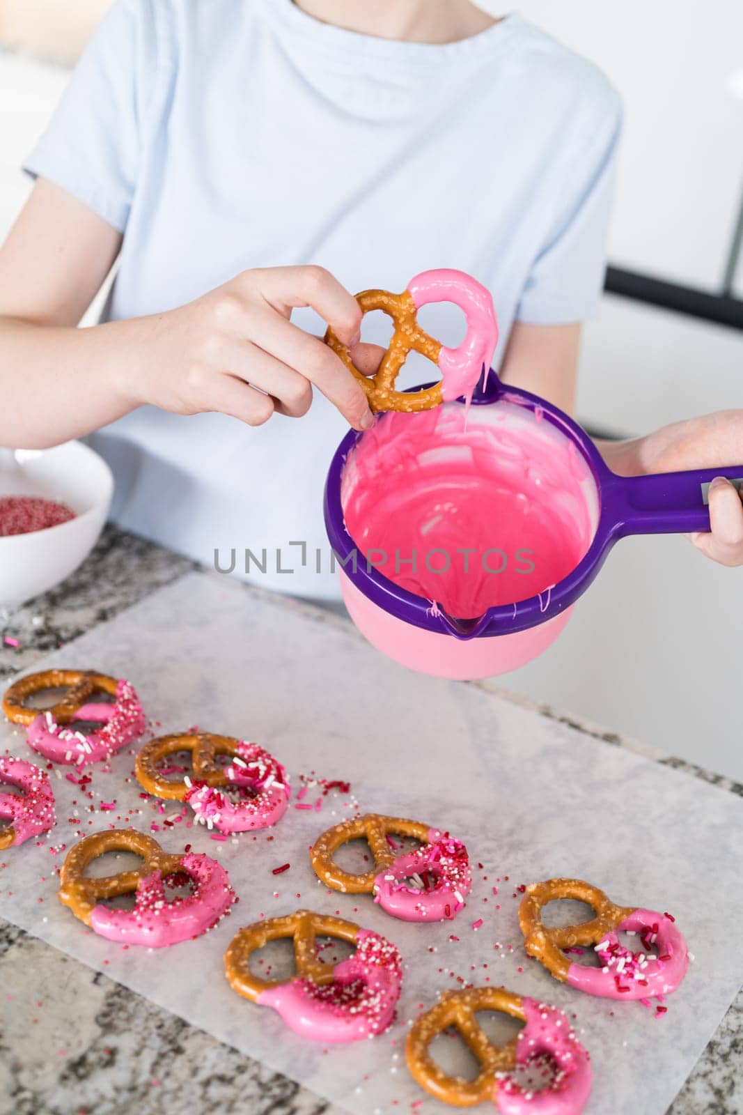 Freshly dipped and still glistening, these crunchy pretzels are lovingly adorned with pink chocolate and a scattering of colorful sprinkles, promising a feast for the senses.