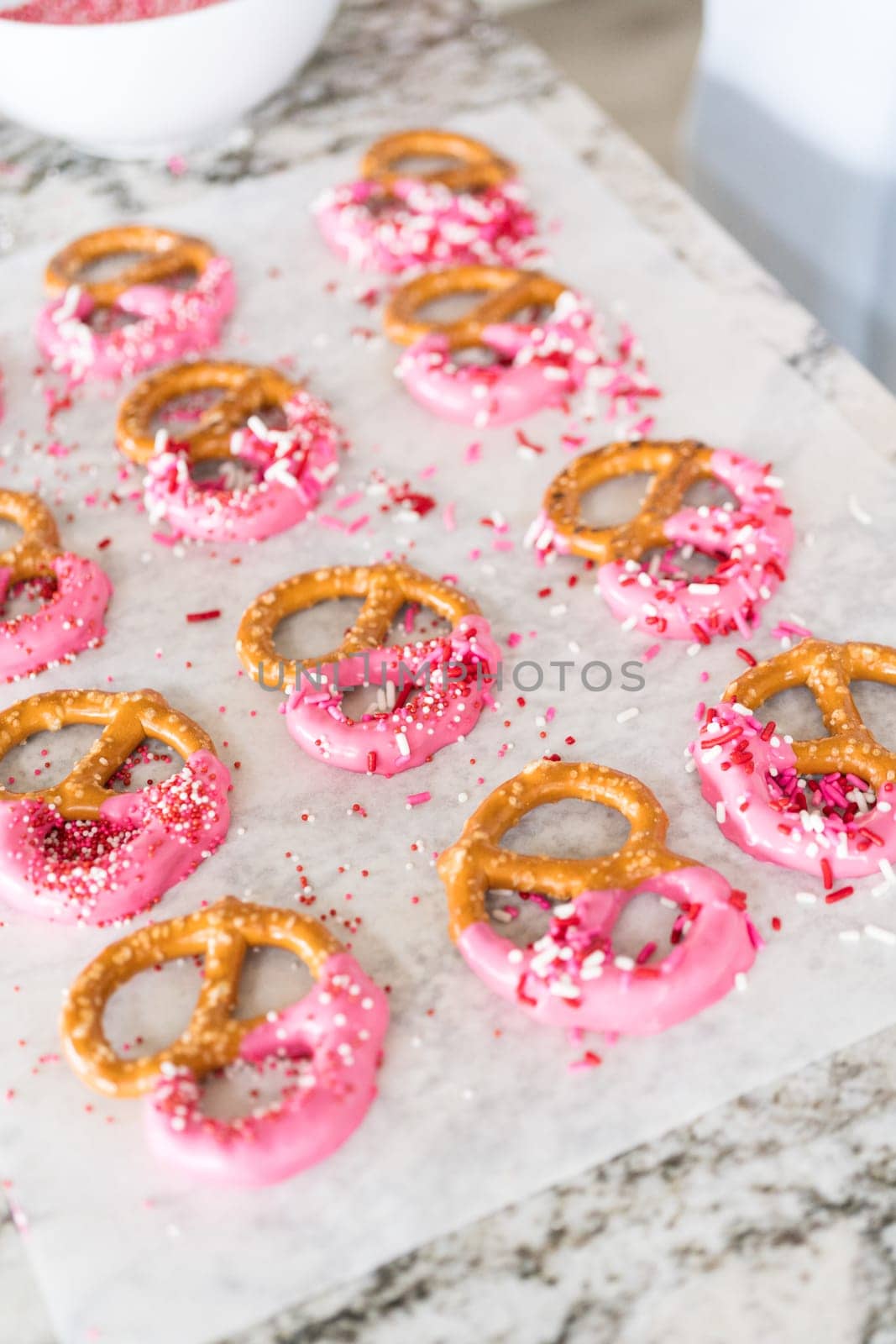 Freshly dipped and still glistening, these crunchy pretzels are lovingly adorned with pink chocolate and a scattering of colorful sprinkles, promising a feast for the senses.