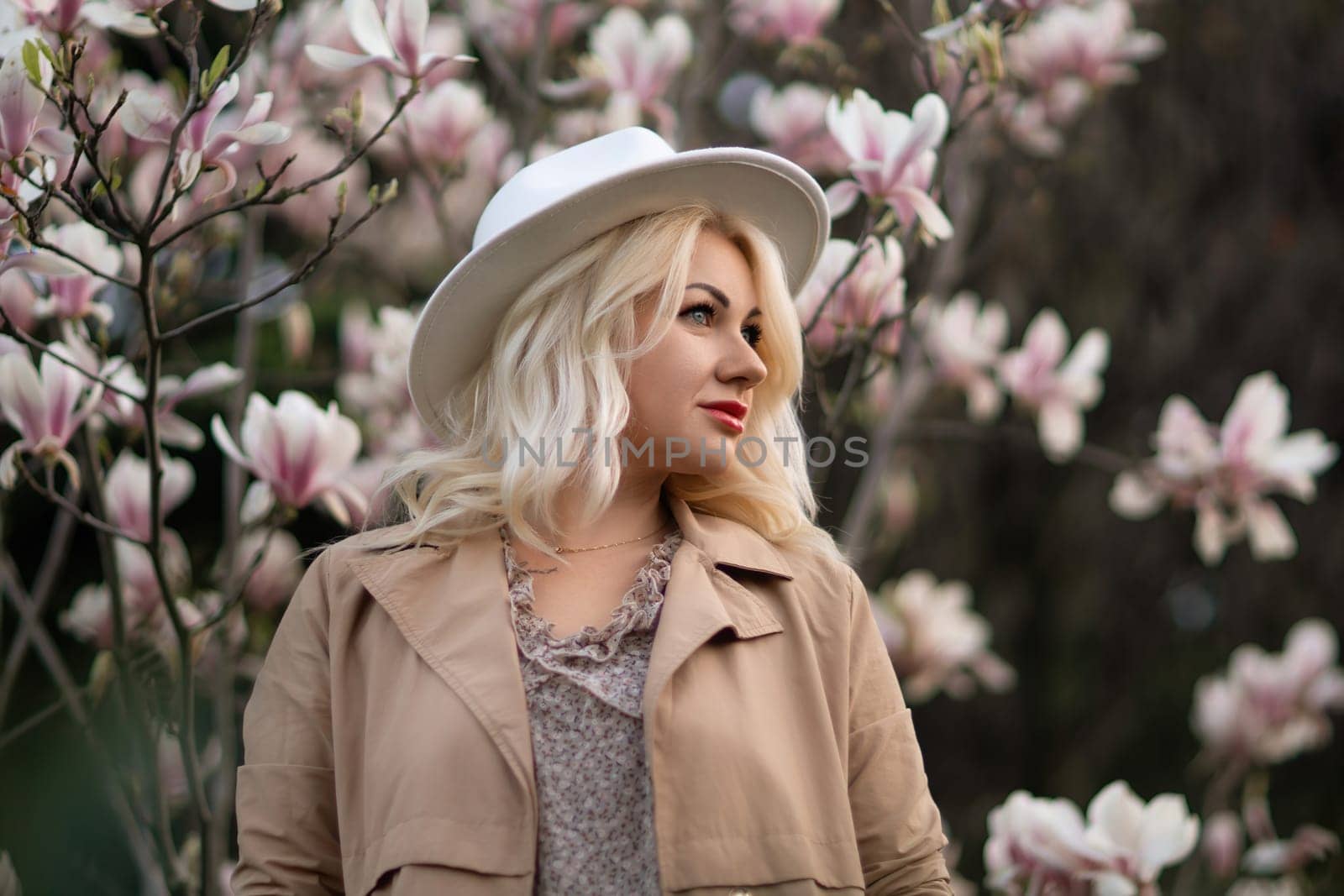 A blonde woman wearing a white hat stands in front of a tree with pink flowers by Matiunina