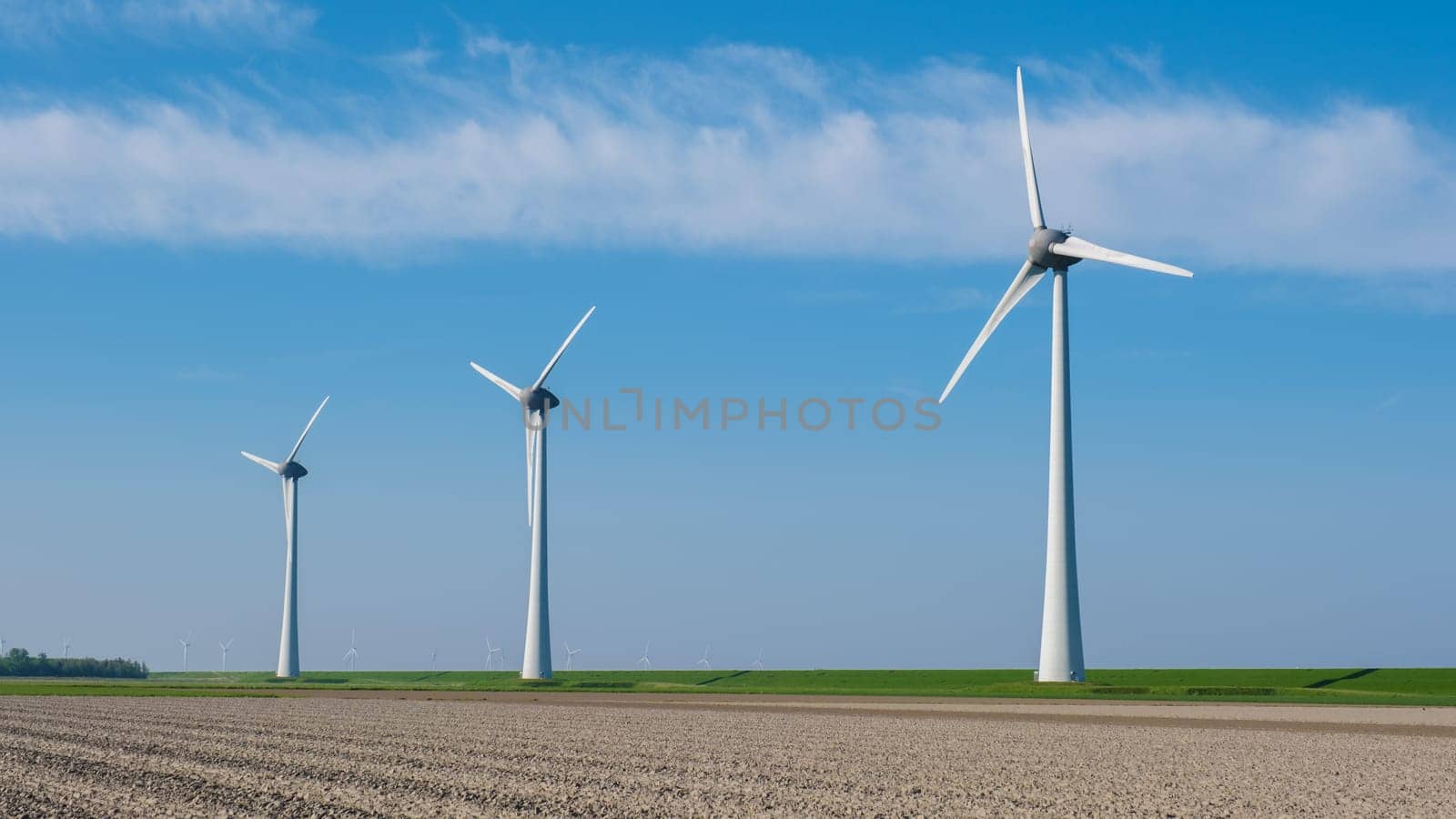 A row of sleek wind turbines stands tall in a vast field in Flevoland, the Netherlands, harnessing the power of the wind to generate renewable energy.