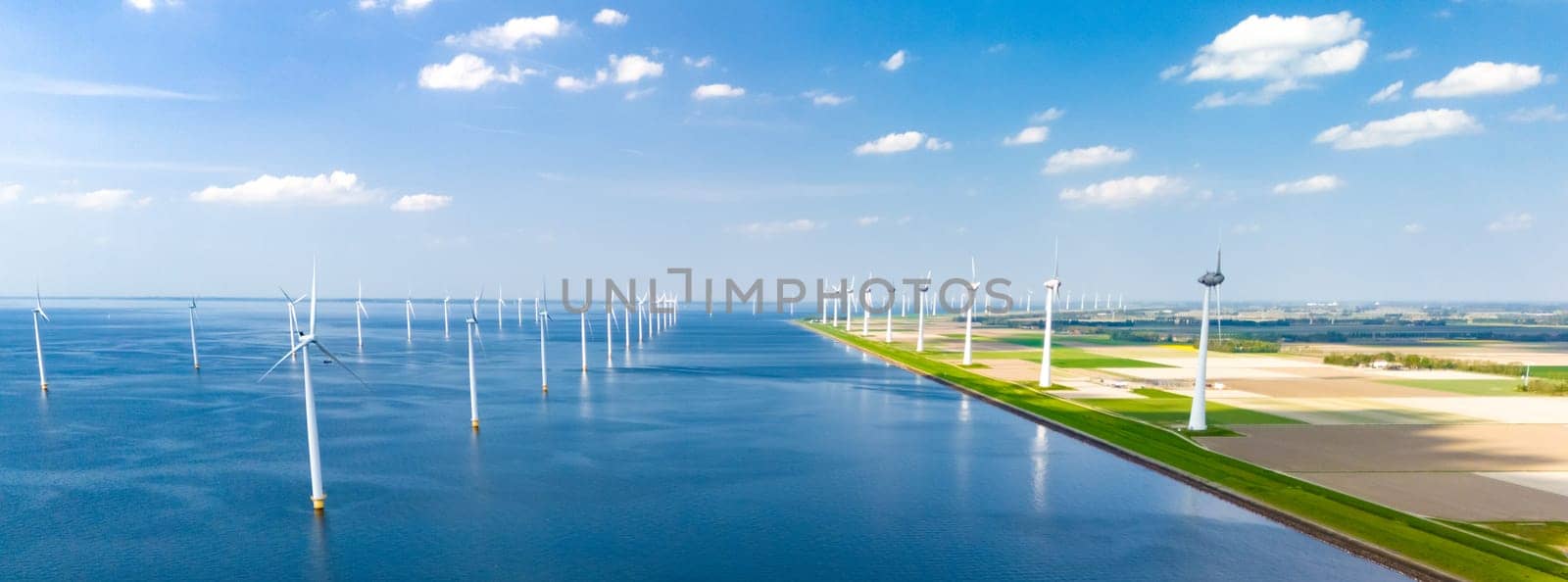 A breathtaking scene of large windmill turbines standing tall around a serene body of water in Flevoland, the Netherlands by fokkebok