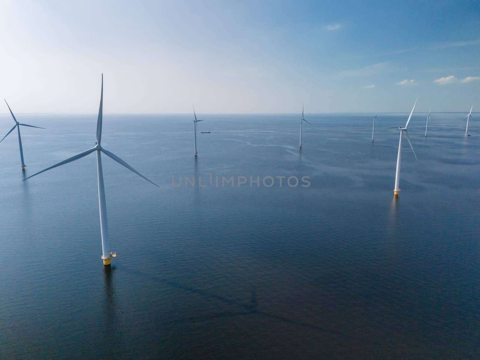 A group of windmills with turbine blades peacefully float atop the calm waters of Flevoland, Netherlands, creating a harmonious and picturesque scene by fokkebok