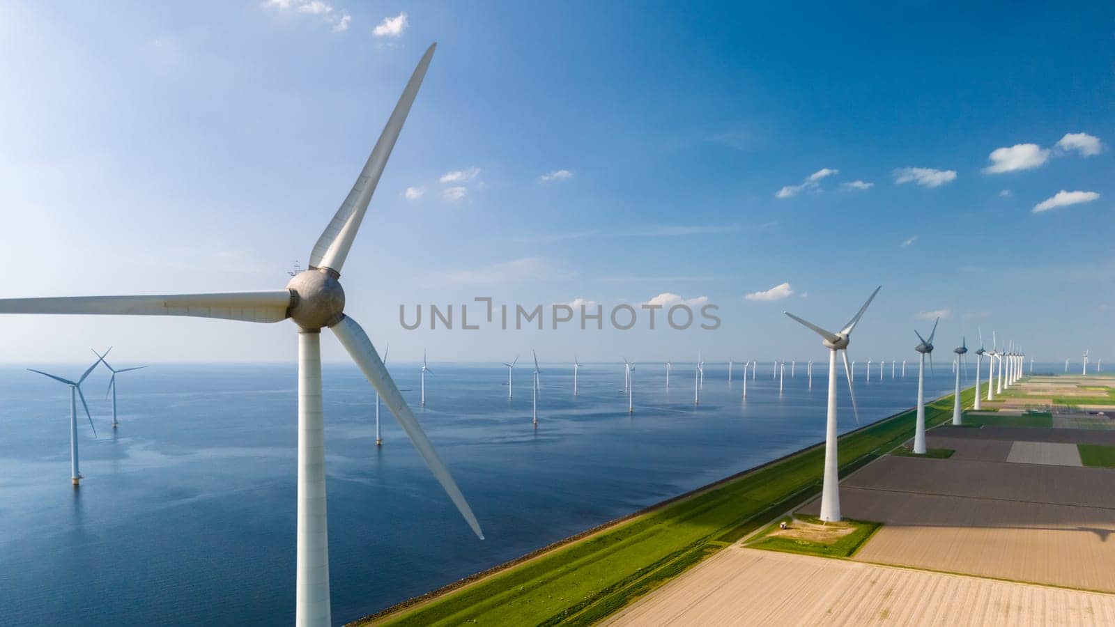 A row of wind turbines stands tall next to a serene body of water, their blades spinning gracefully in the wind, generating clean energy.