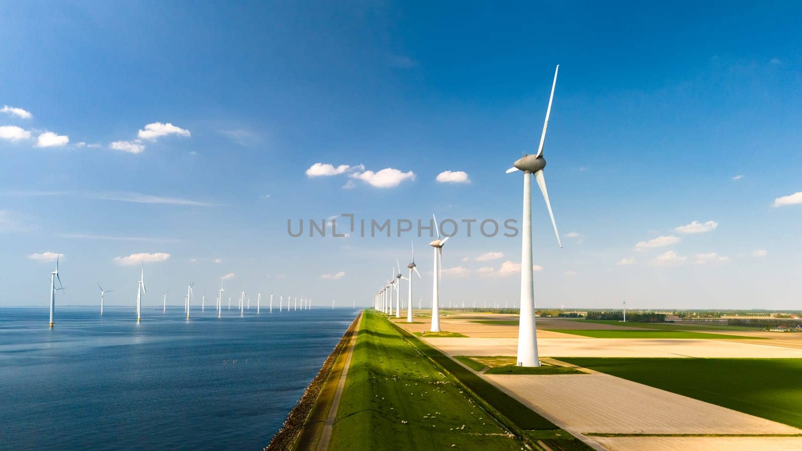 A row of towering wind turbines gracefully spin with the breeze next to a tranquil body of water in the Netherlands Flevoland region. Energy transition in Europe