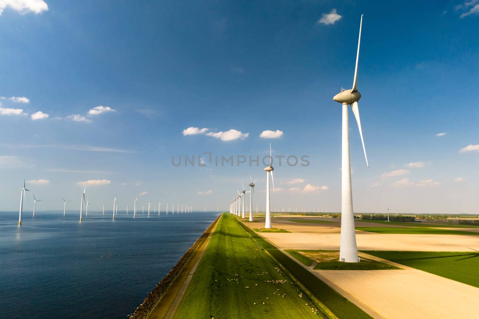 A row of elegant wind turbines stand tall next to a serene body of water, harnessing the power of the wind to generate renewable energy by fokkebok