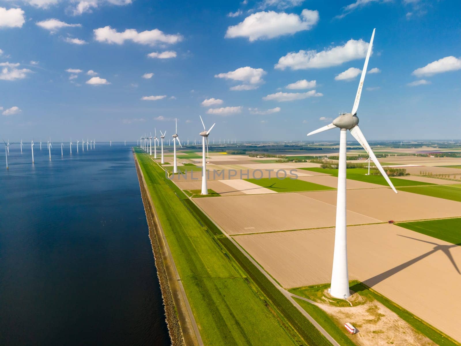 A mesmerizing landscape of wind turbines gracefully spinning in a wind farm by a serene body of water, showcasing sustainable energy production by fokkebok