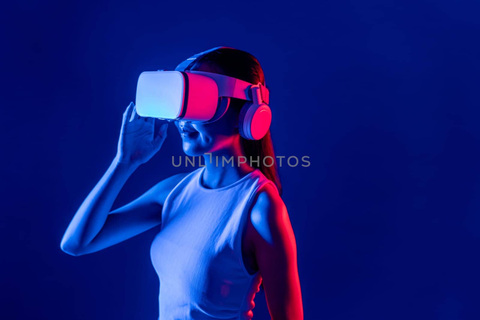 Smart female stand with surrounded by cyberpunk neon light wear VR headset connecting metaverse, futuristic cyberspace community technology. Elegant woman look generated virtual area. Hallucination.