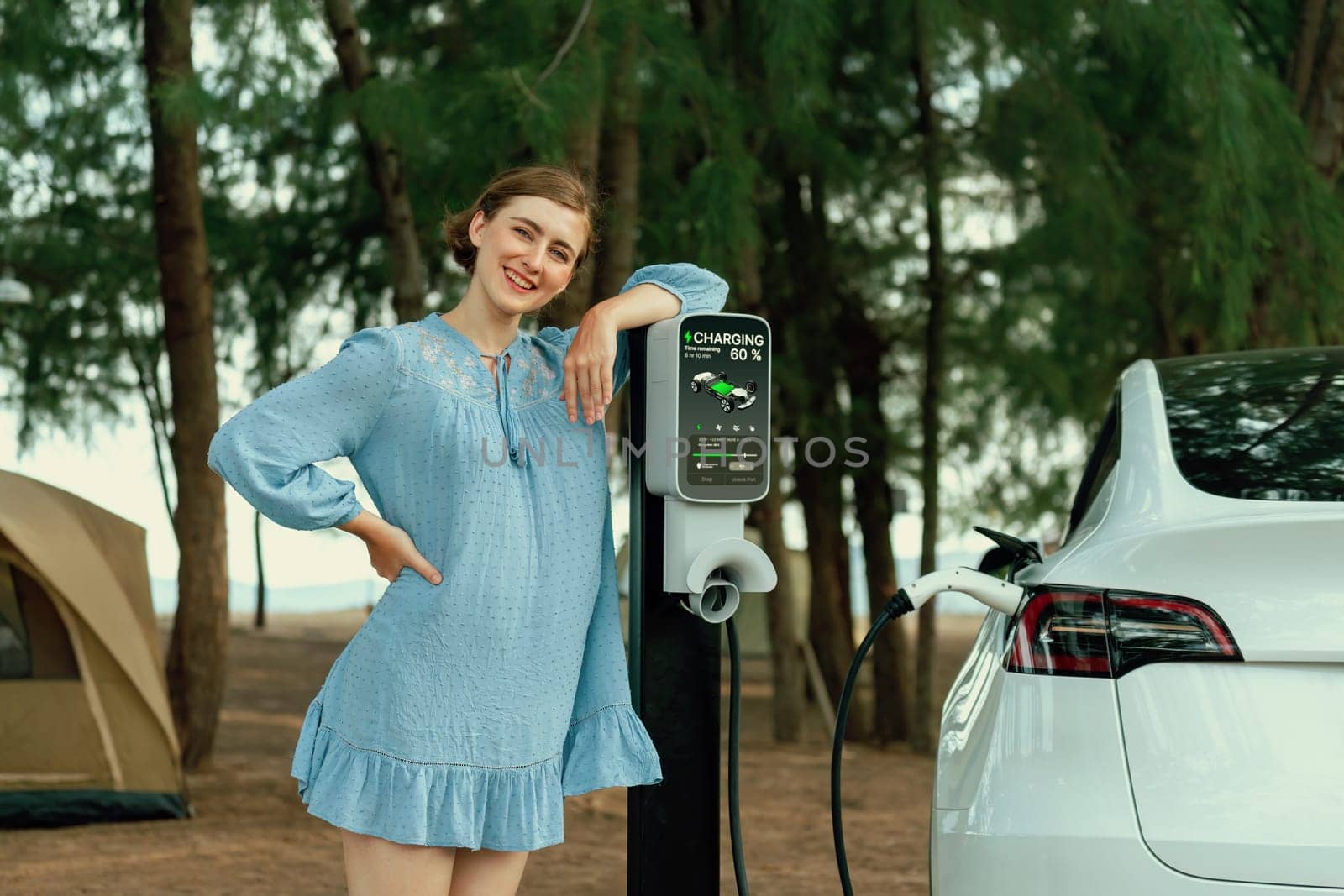 Holiday road trip vacation traveling to the beach camp with electric car, young woman recharge EV vehicle with green and clean energy. Beach travel camping with eco-friendly EV car .Perpetual