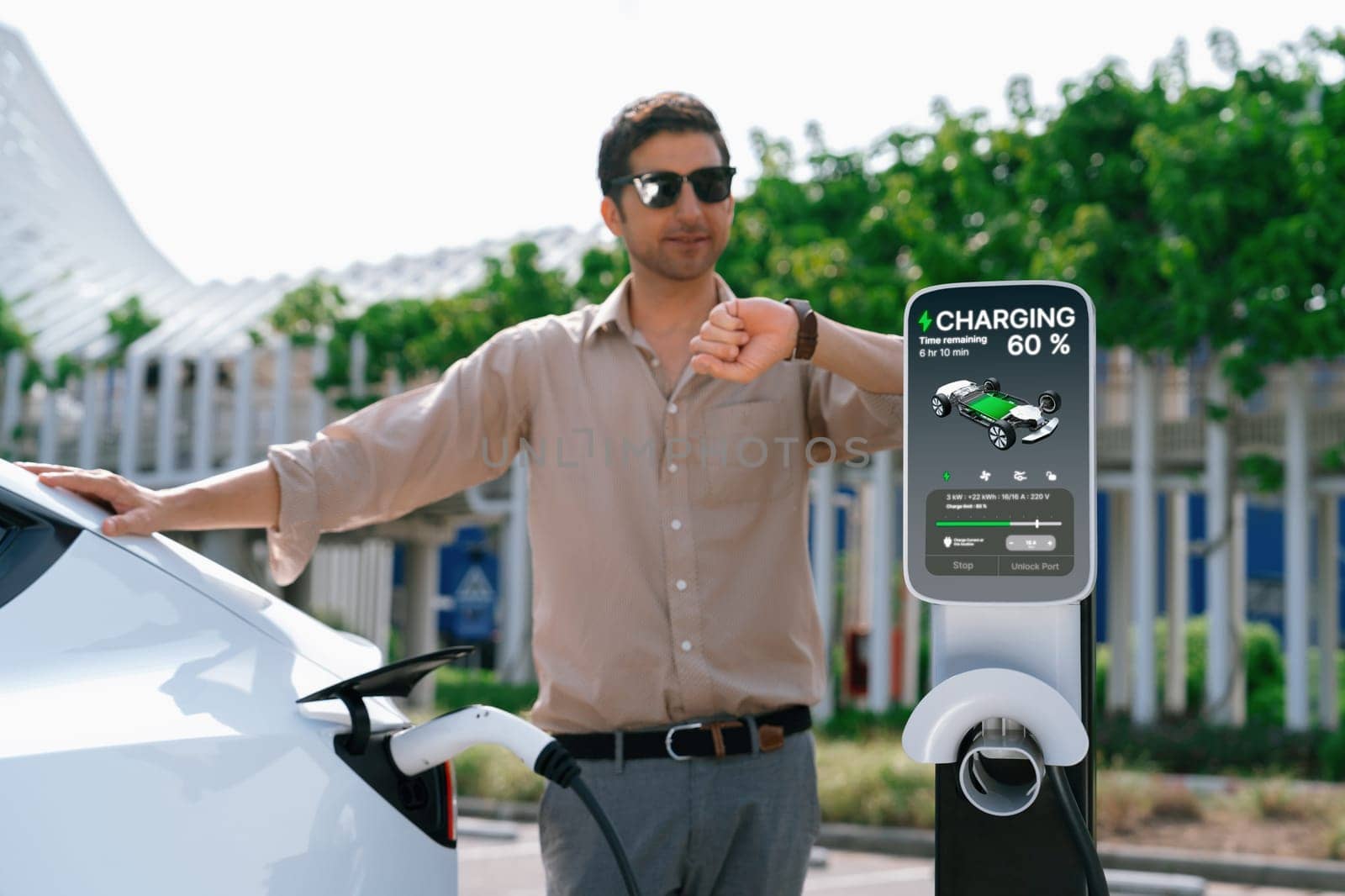 Young man put EV charger to recharge electric car's battery from charging station in city commercial parking lot. Rechargeable EV car for sustainable environmental friendly urban travel. Expedient