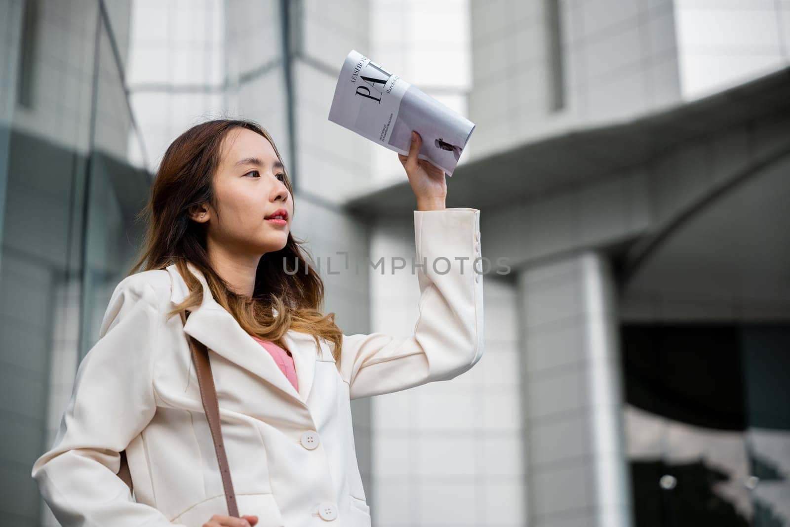 Businesswoman walking out the building after finish work shade sun UV with newspaper. Portrait of Young Asian woman wearing white shirt while cover the sun by news paper on the streets of downtown