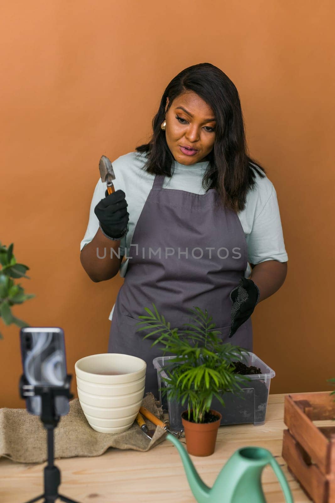 African american florist blogger filming tutorial video about transplanting plants in home garden. Make video vlog with mobile phone by Satura86