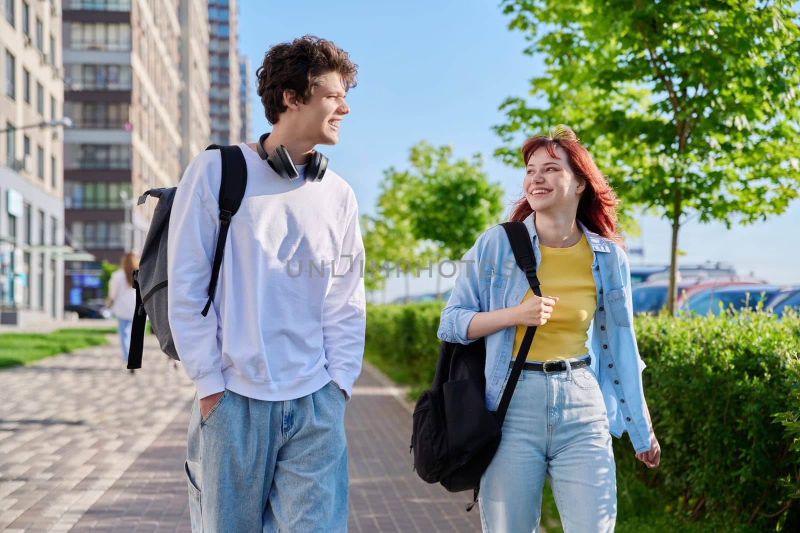 Guy and girl, university students walking together along street of city by VH-studio