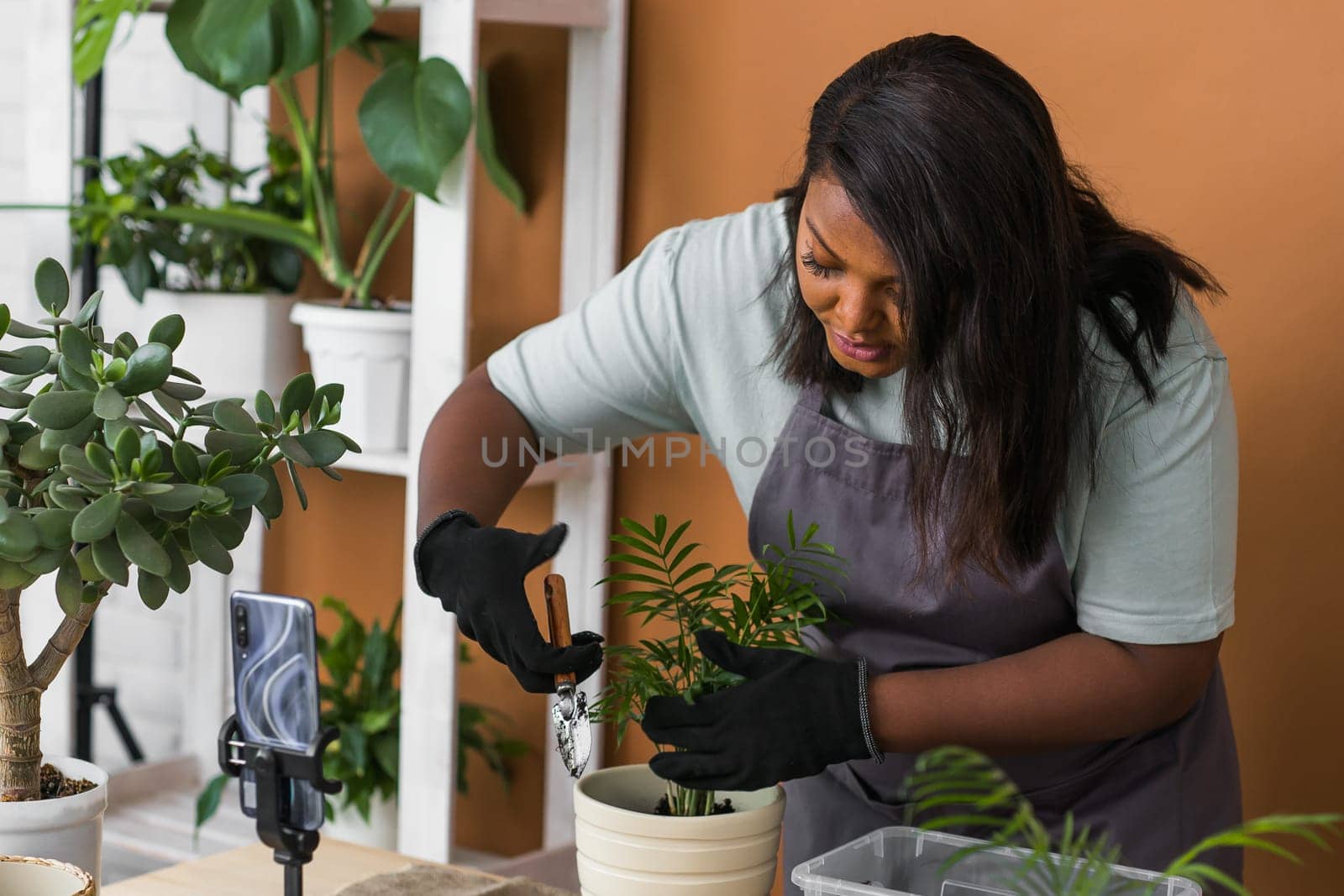 African american florist blogger filming tutorial video about transplanting plants in home garden. Make video vlog with mobile phone concept