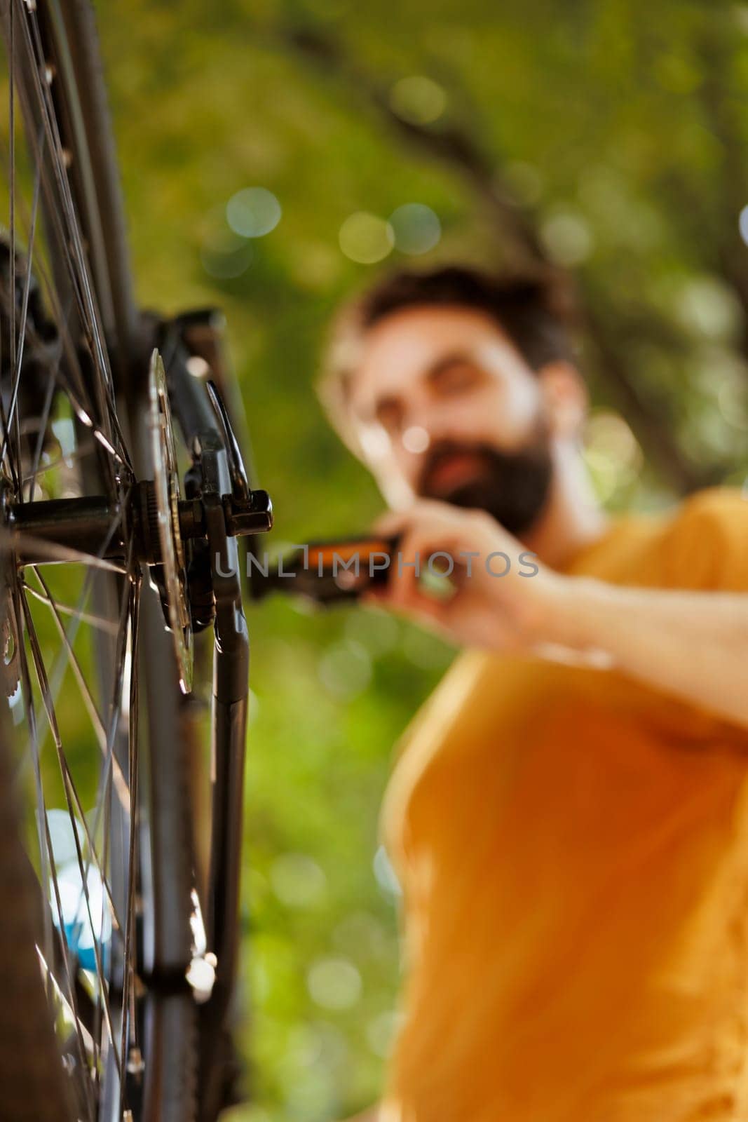 Image showing close-up view of bike rear derailleur and cogset being repaired and adjusted outside for leisure cycling. Detailed shot of young male cyclist checking tire as annual bike maintenance routine.