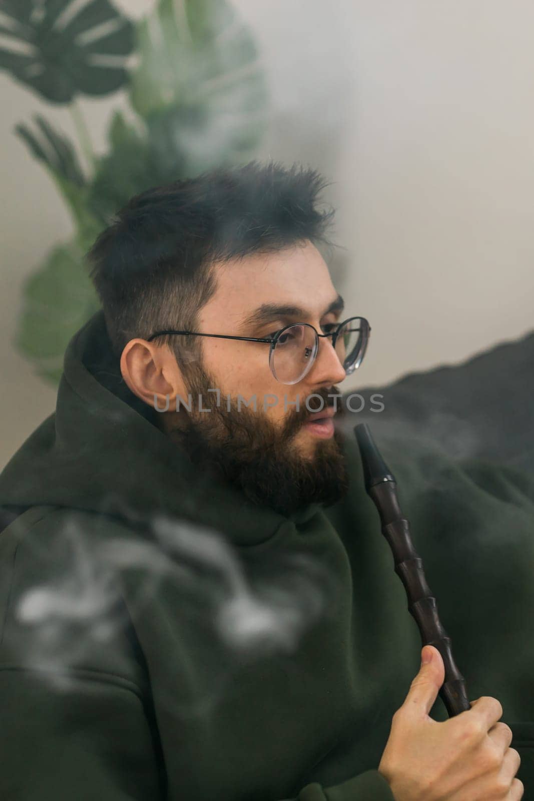 Bearded man is smoking hookah at home and blowing cloud of smoke - chill time and resting concept by Satura86