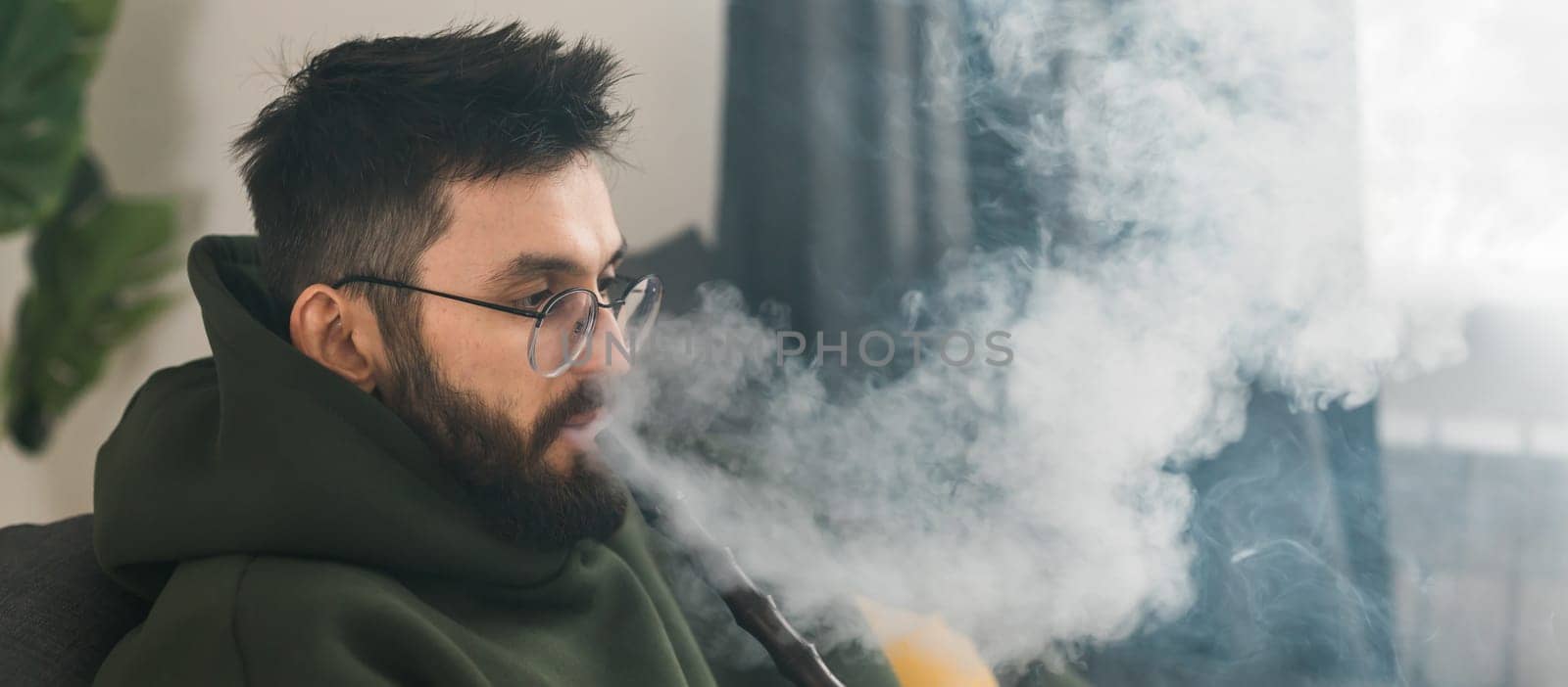 Banner bearded millennial or gen z man smoking hookah while relaxing on sofa at home copy space - chill time and resting concept by Satura86
