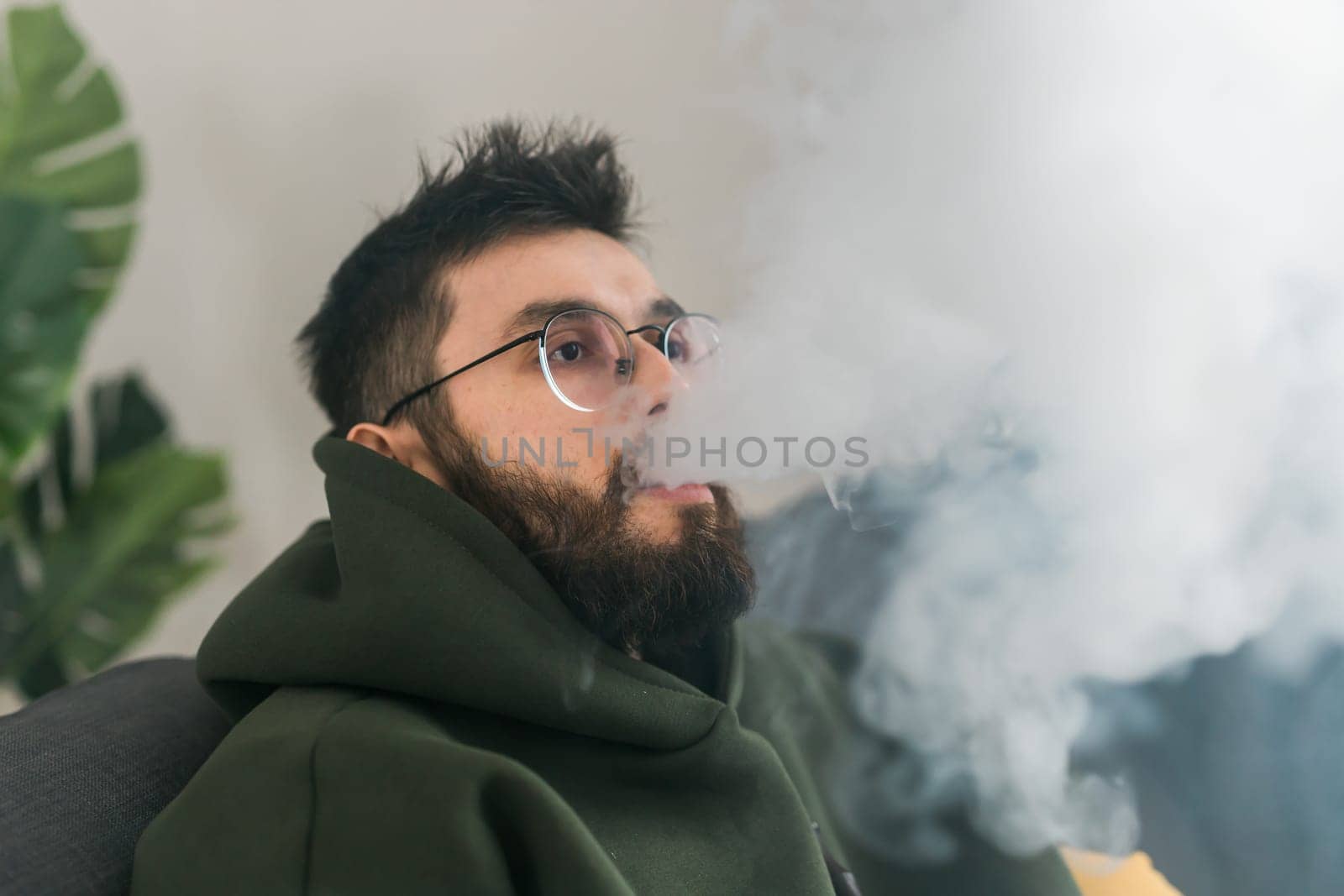 Portrait bearded man is smoking hookah at home and blowing cloud of smoke, copy space and place for text - chill time and resting concept by Satura86