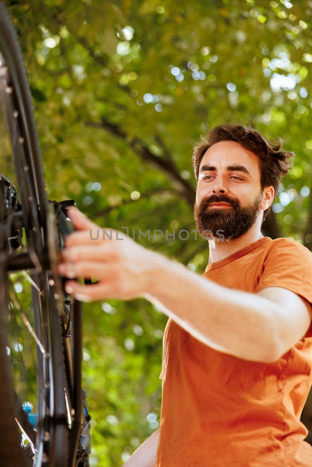 Close-up of young healthy caucasian man examining and adjusting bike wheel rubber and chain outside. Image showing enthusiastic sporty male working on bicycle chain ring in home yard.