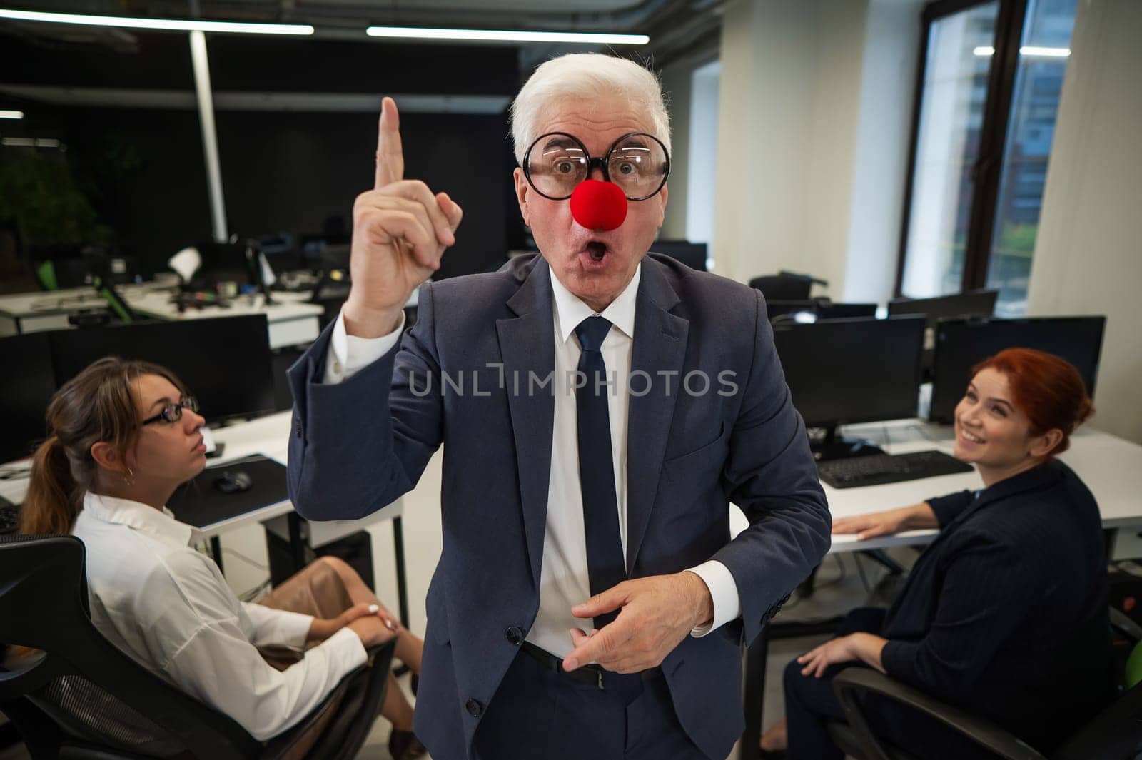 An elderly man in a clown costume fools around at work. by mrwed54