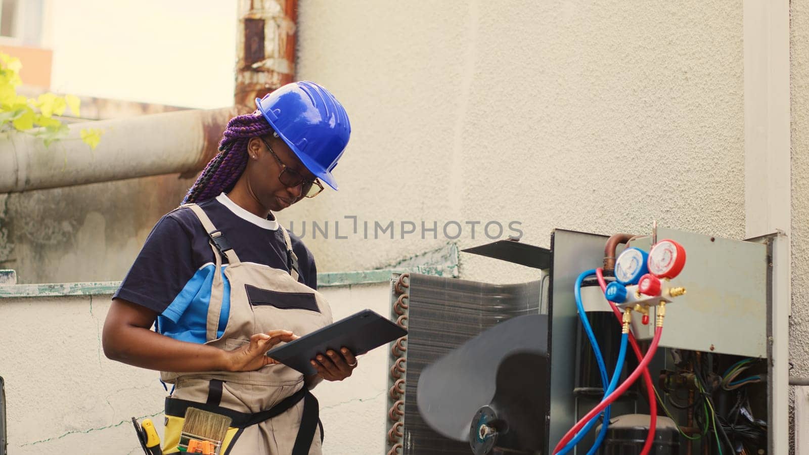 Seasoned mechanic servicing external condenser internal parts, checking refrigerant level and calibrating thermostats. Capable electrician imputing maintenance results data on laptop