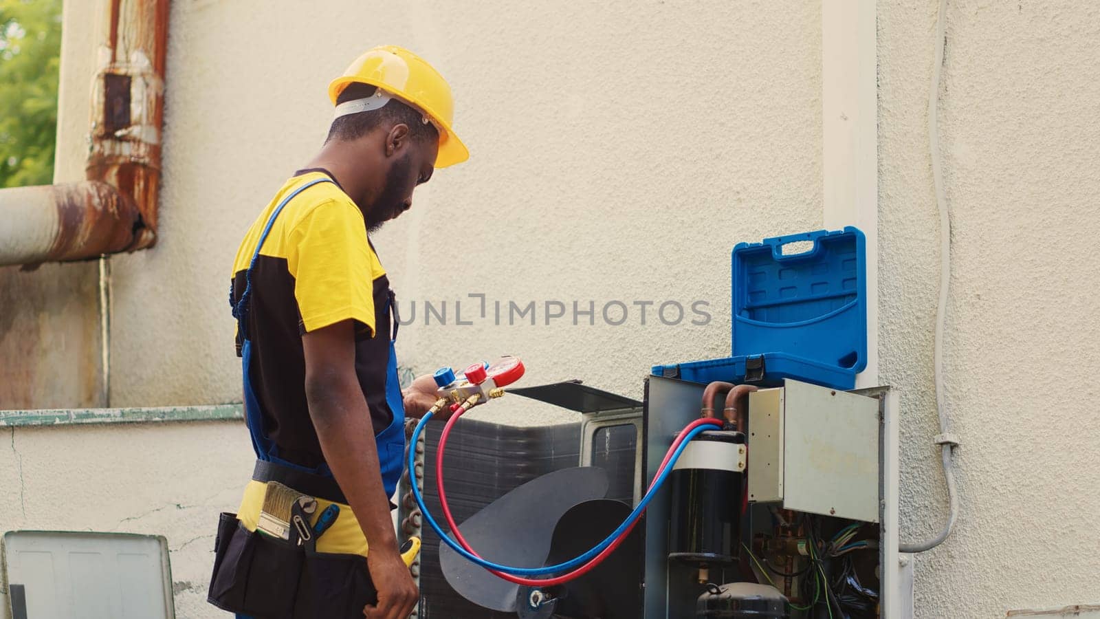 Qualified mechanic looking at freon levels in external air conditioner while using manifold meters to meticulously measure the pressure in condenser, ensuring efficient cooling performance