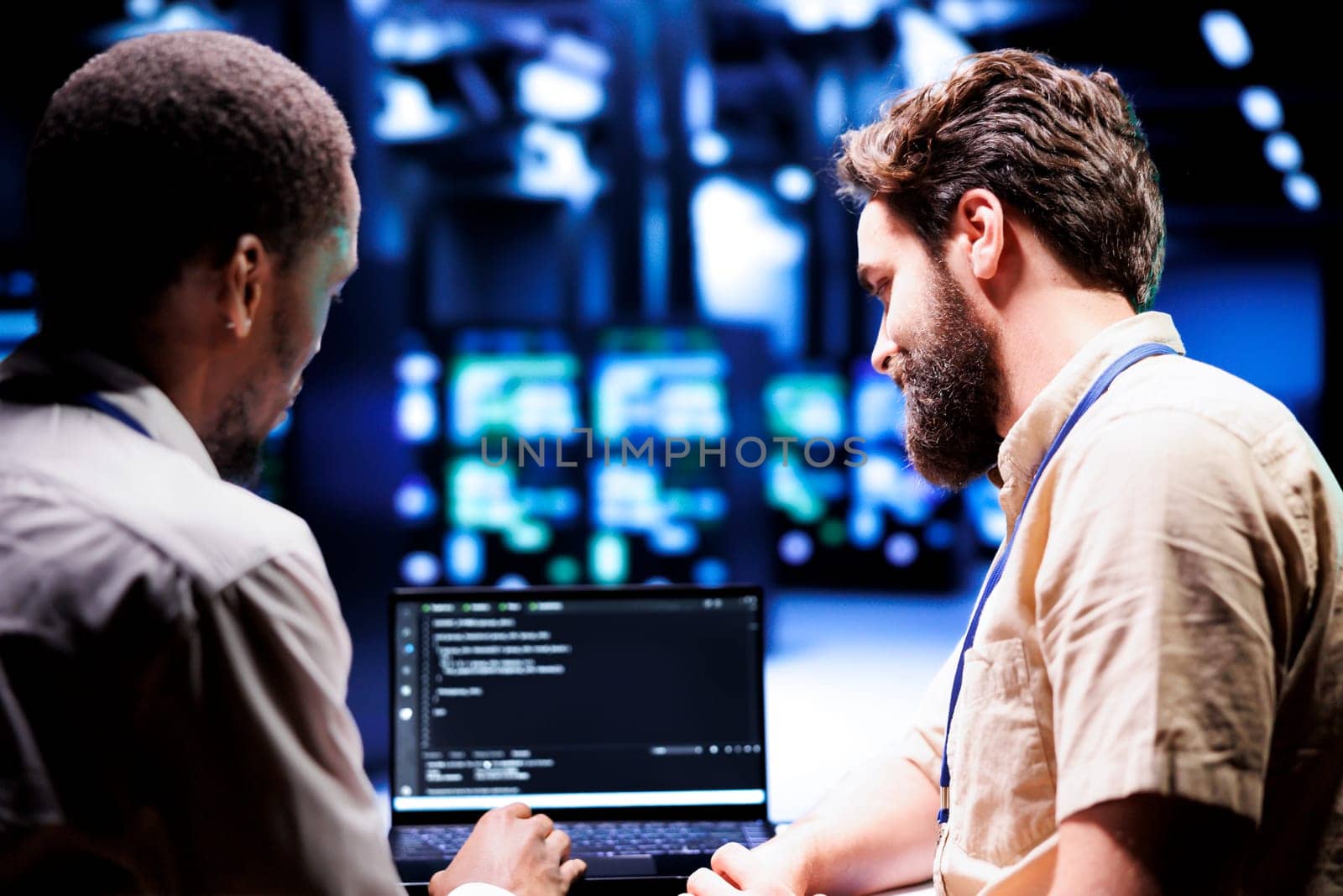 IT developers collaborating in server farm writing script code on laptop terminals. Programmers team conducting maintenance tasks in highly advanced data center, ensuring racks software is up to date