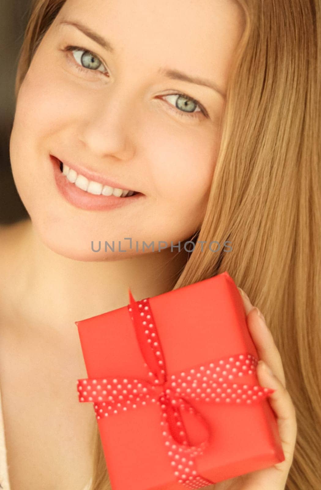 Happy smiling woman holding a red gift box, face portrait with natural make-up and holiday lifestyle at home concept