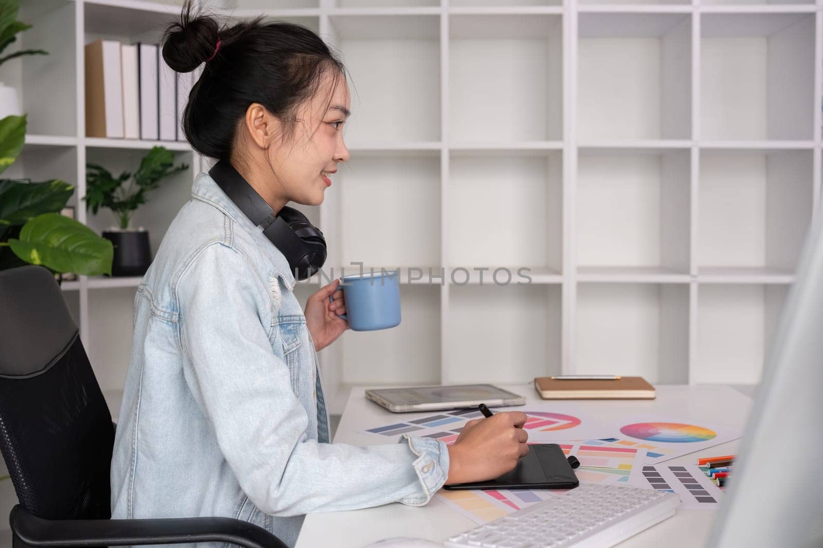 Female designer wearing headphones listening to music while doing graphic design work Choose colors for working with the computer at the table..