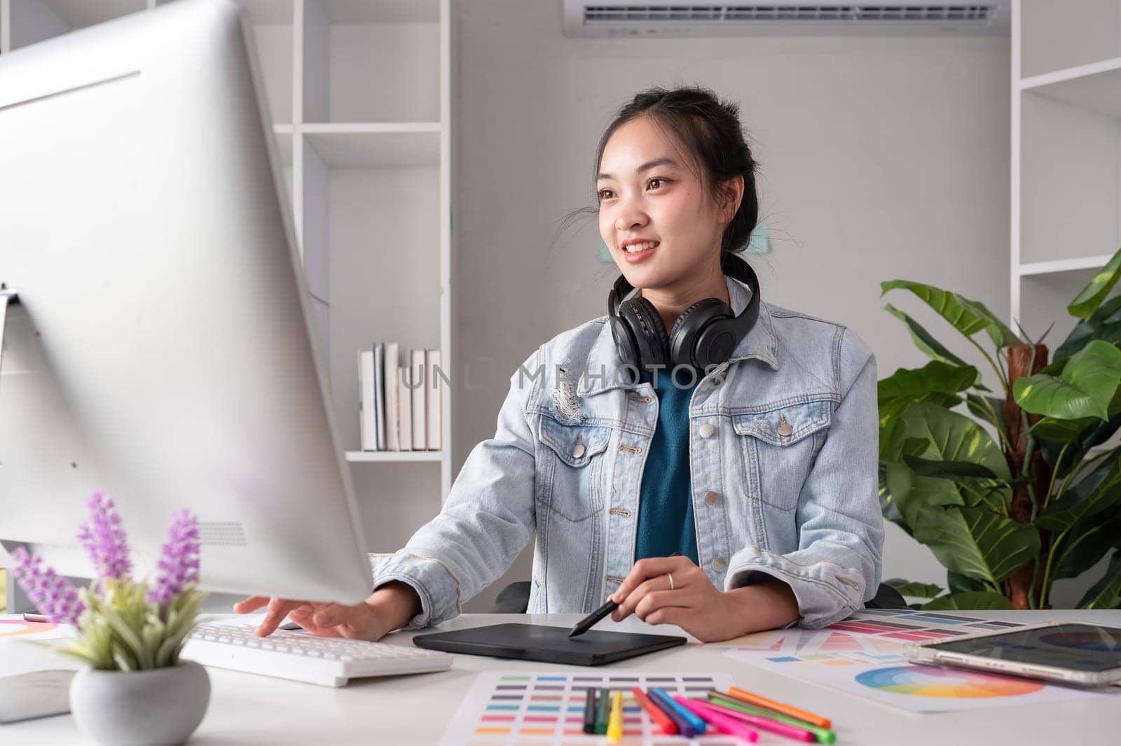 Female designer wearing headphones listening to music while doing graphic design work Choose colors for working with the computer at the table. by wichayada