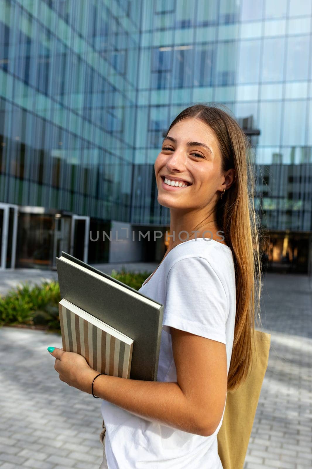 Vertical portrait of happy smiling blonde female college student looking at camera holding notebooks. by Hoverstock