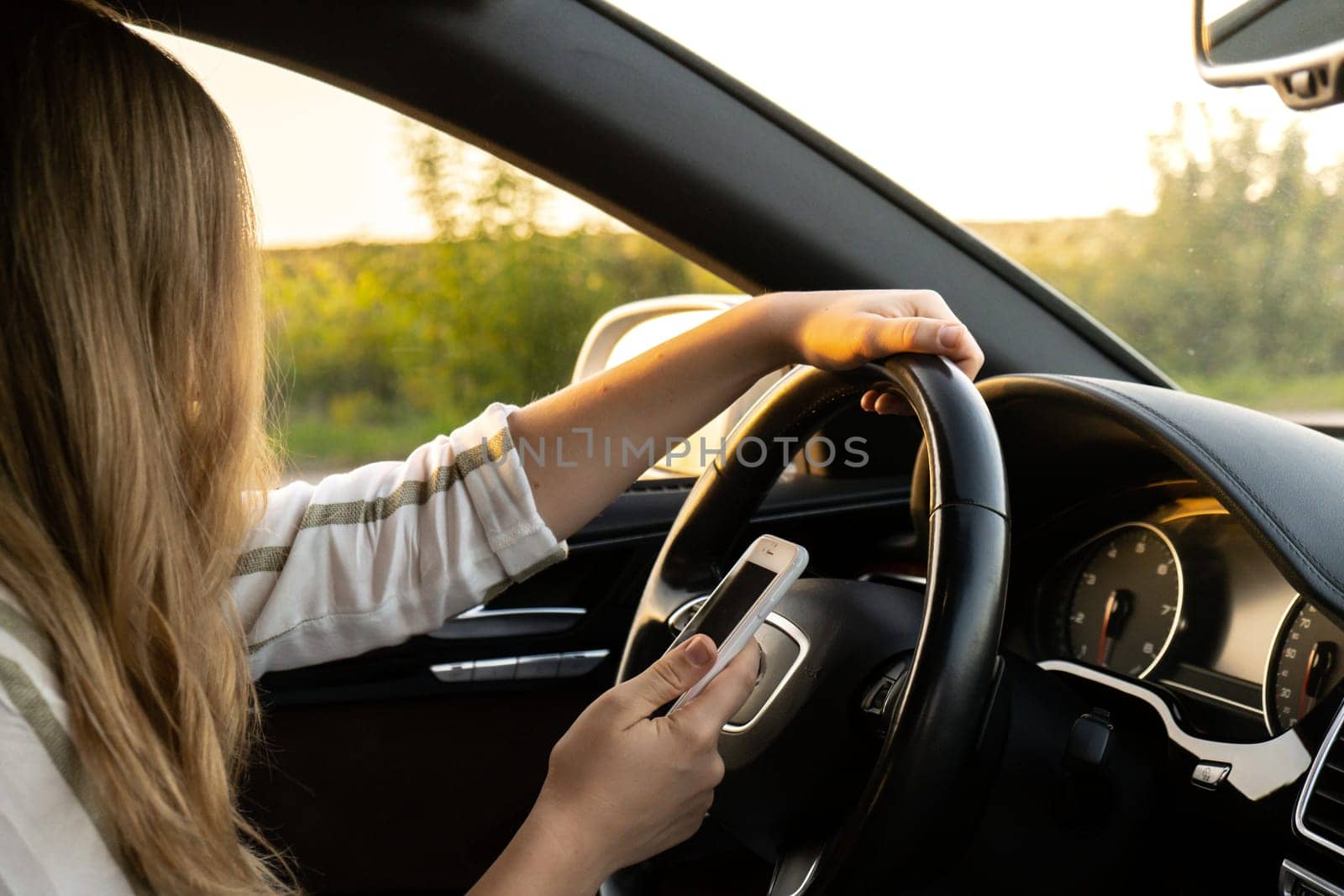 Woman sending messages with smartphone while driving automobile. Female driver using mobile phone on the road during driving the car. Safety and technology by anna_stasiia