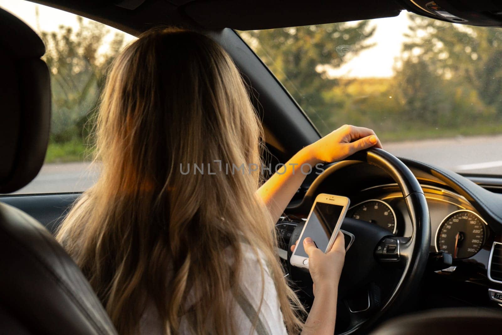 Woman sending messages with smartphone while driving automobile. Female driver using mobile phone on the road during driving the car. Safety and technology concept