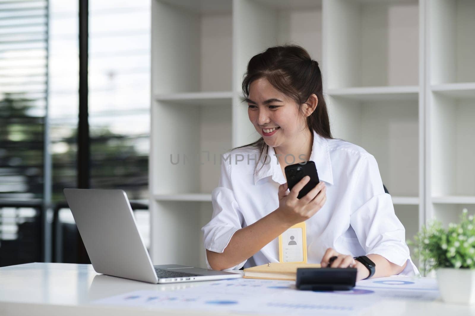 Business Caucasian woman Talking on the phone and using a laptop with a smile while sitting at modern office by wichayada