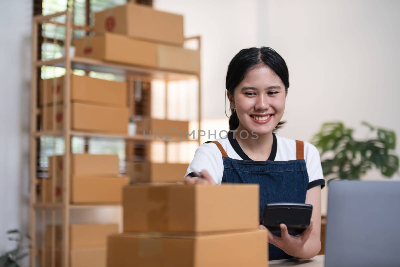 Young woman, small business owner selling products online, accepting online product orders via laptop, sits in a room with boxes of products..