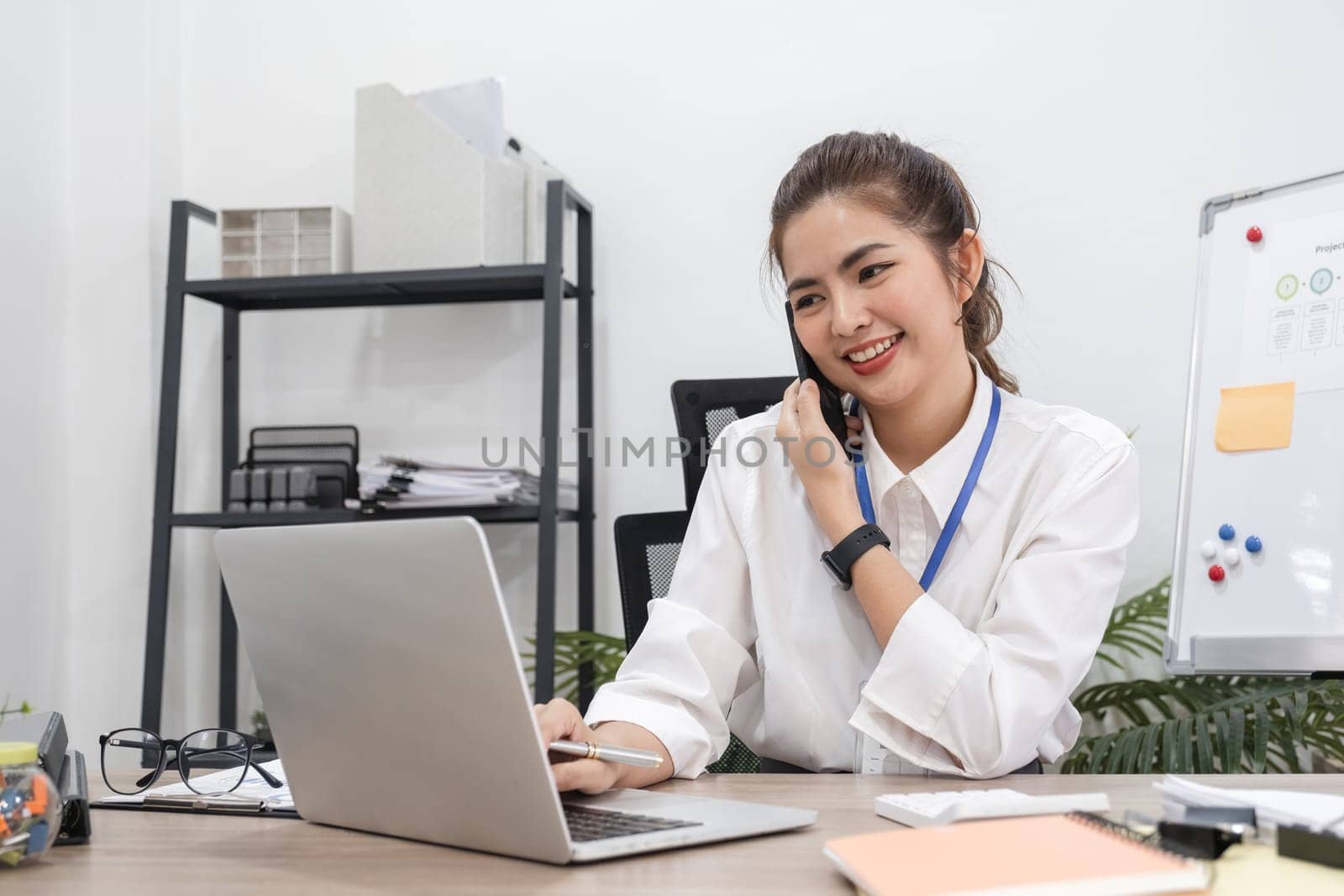 Beautiful business woman working with laptop, recording data and discussing work over the phone in modern office by wichayada