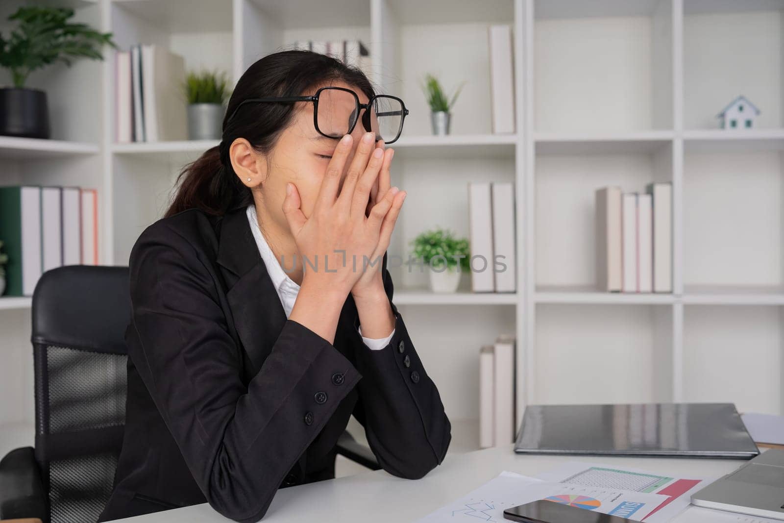 Young Asian businesswoman in the office is disappointed and stressed about her performance in the company. by wichayada