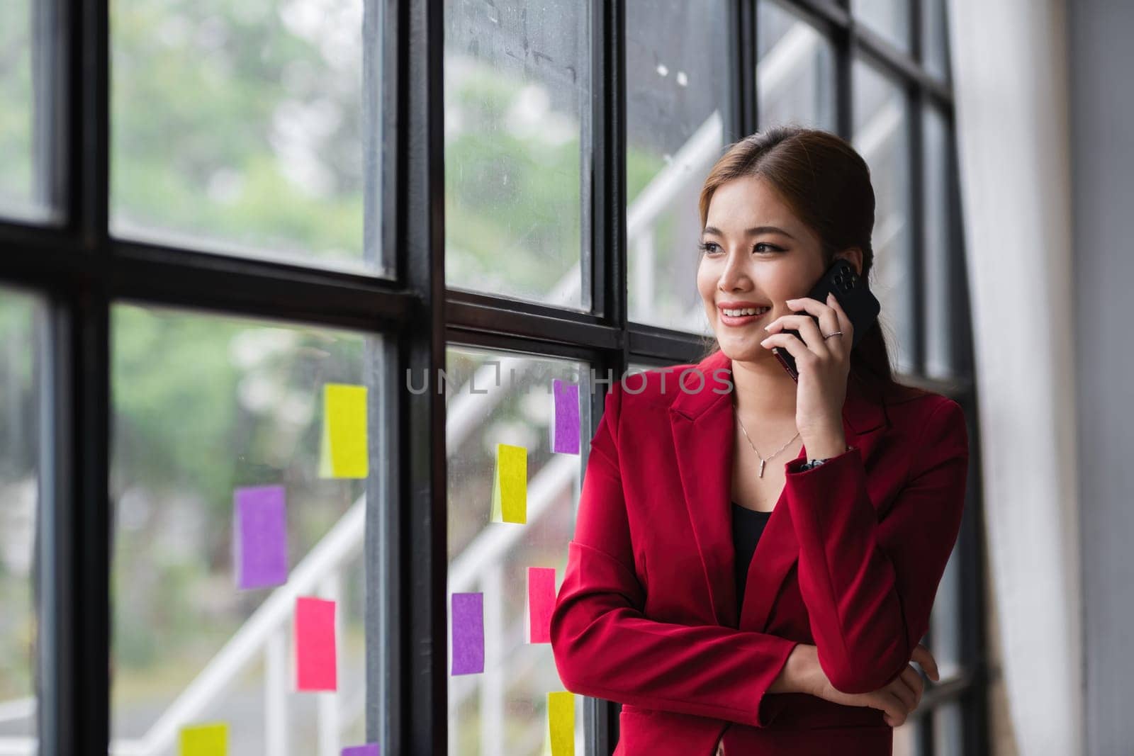 Asian businesswoman talking in a work meeting on the phone, taking notes on sticky notes on the wall in the office.