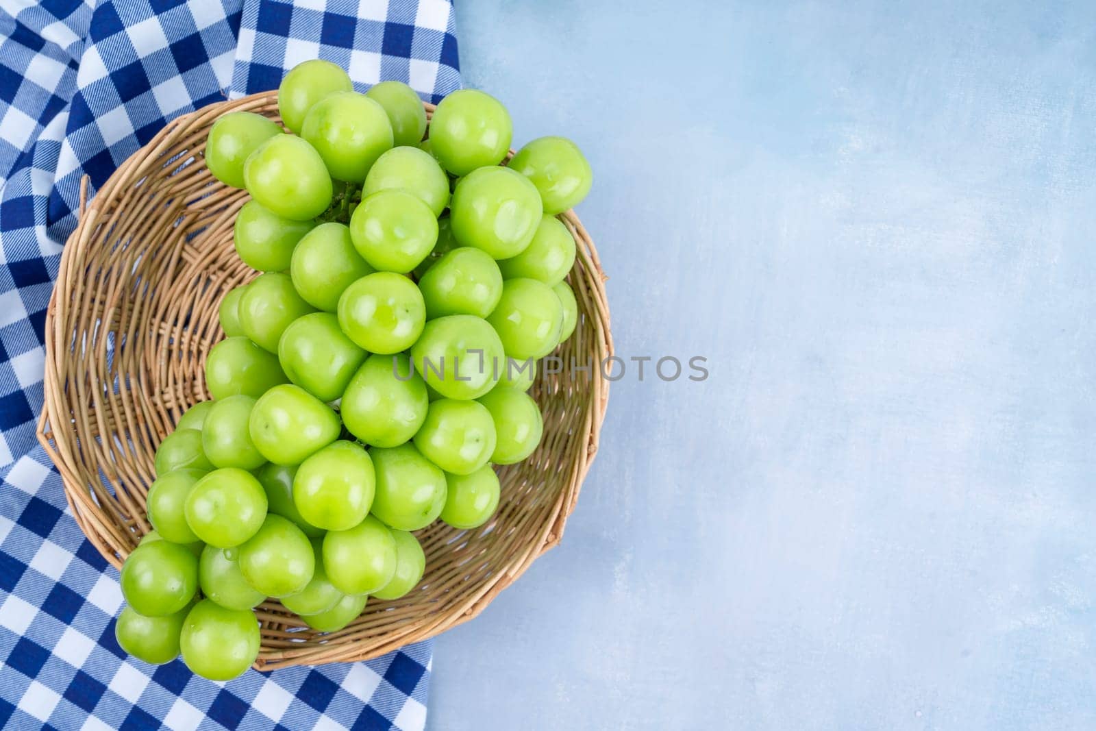 Sweet Green Shine Muscat grape in Bamboo basket with tablecloth on the table with empty space.