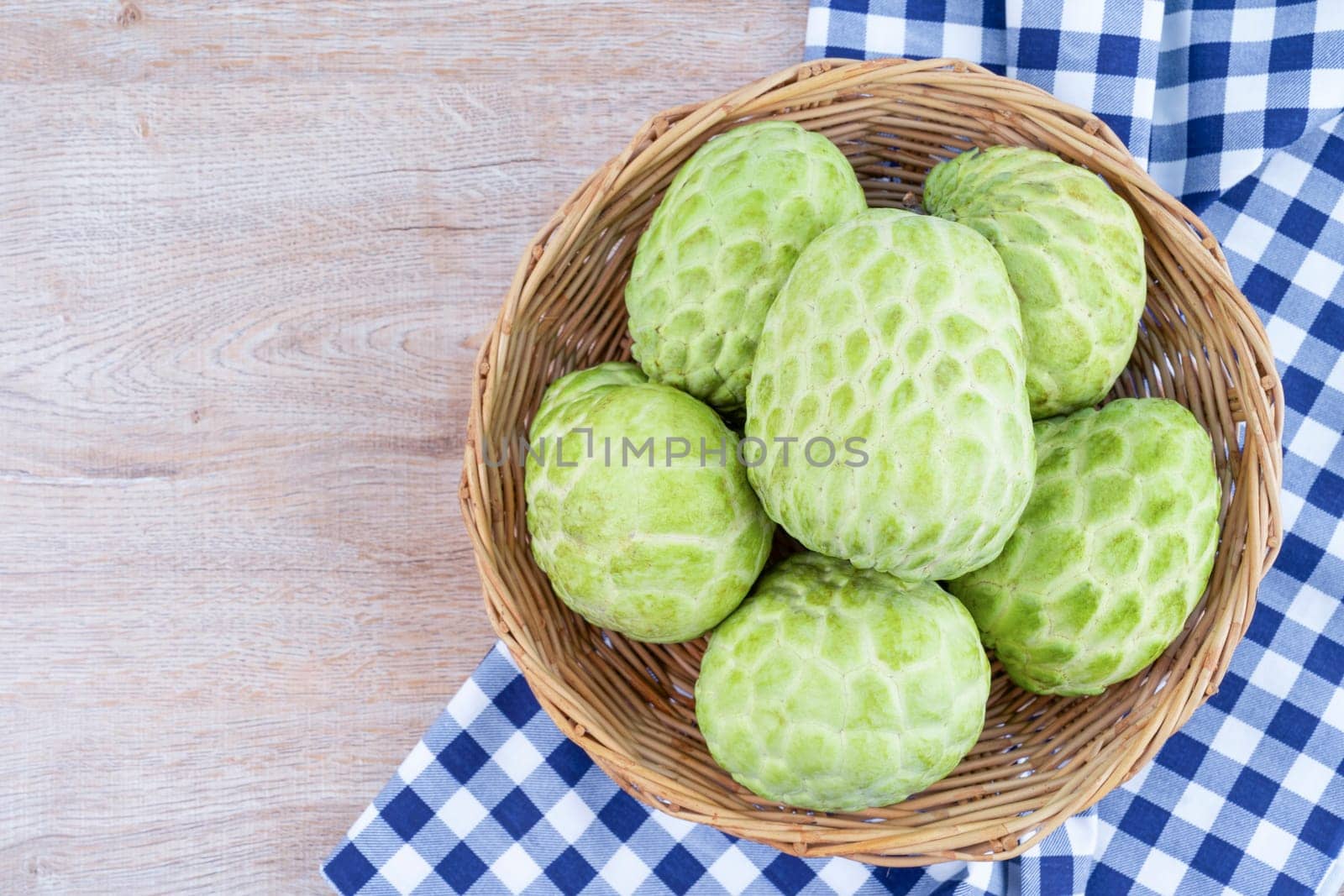The Sugar apples or custard apples in a wooden weave basket on wooden table. by Gamjai