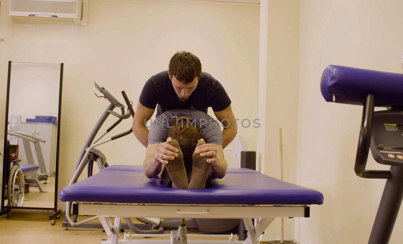 Doctor physiotherapist doing recovery exercises for young disable man at the rehabilitation clinic