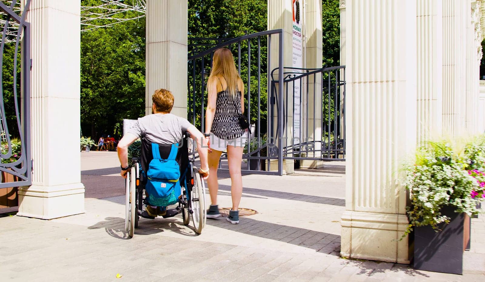 Young disable man in wheelchair walking in the park with his wife. Rear view.