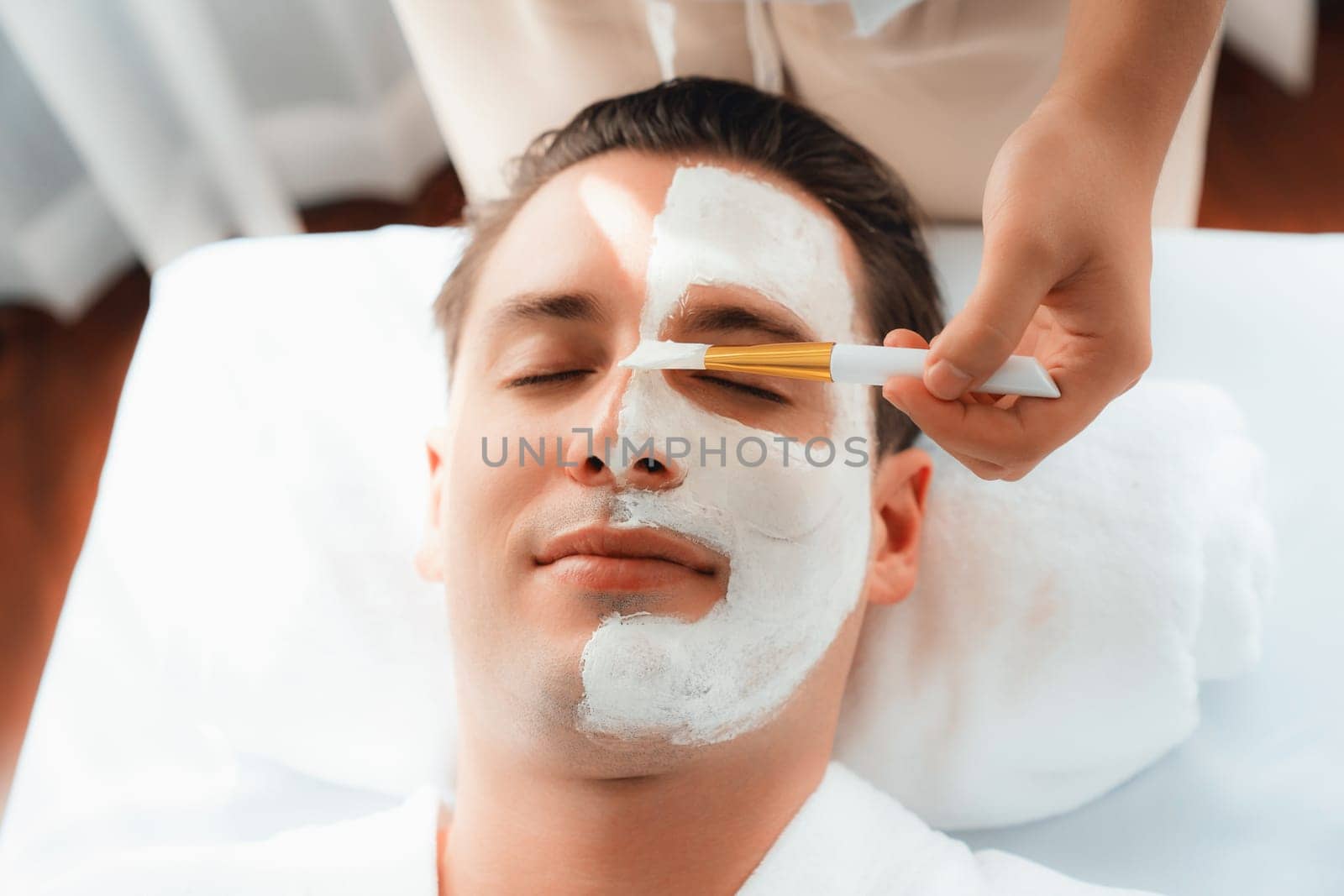 Serene ambiance of spa salon, man customer indulges in rejuvenating with luxurious face cream massage with modern daylight. Facial skin treatment and beauty care concept. Quiescent