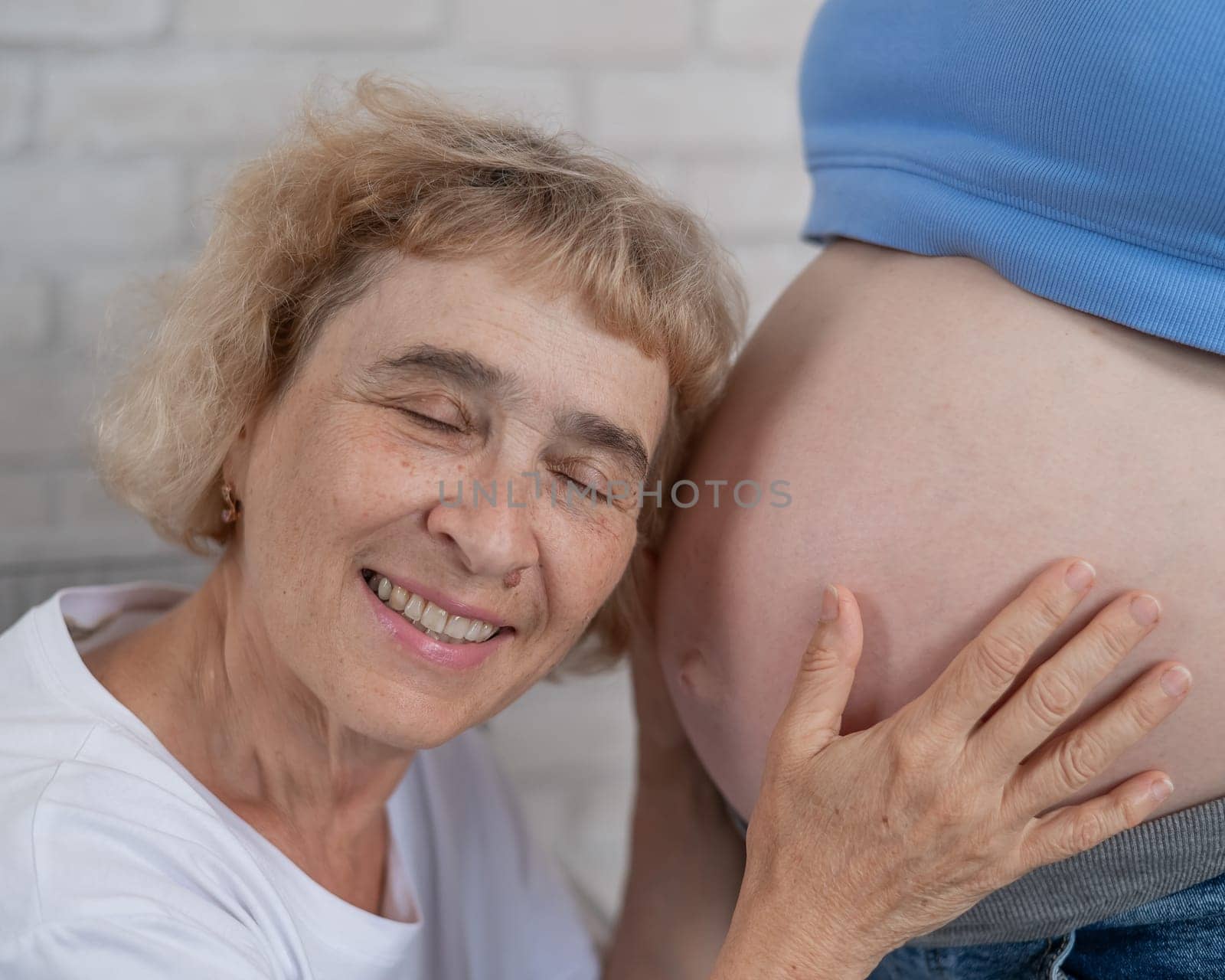 An elderly woman leans against the belly of her pregnant daughter. Close-up. by mrwed54