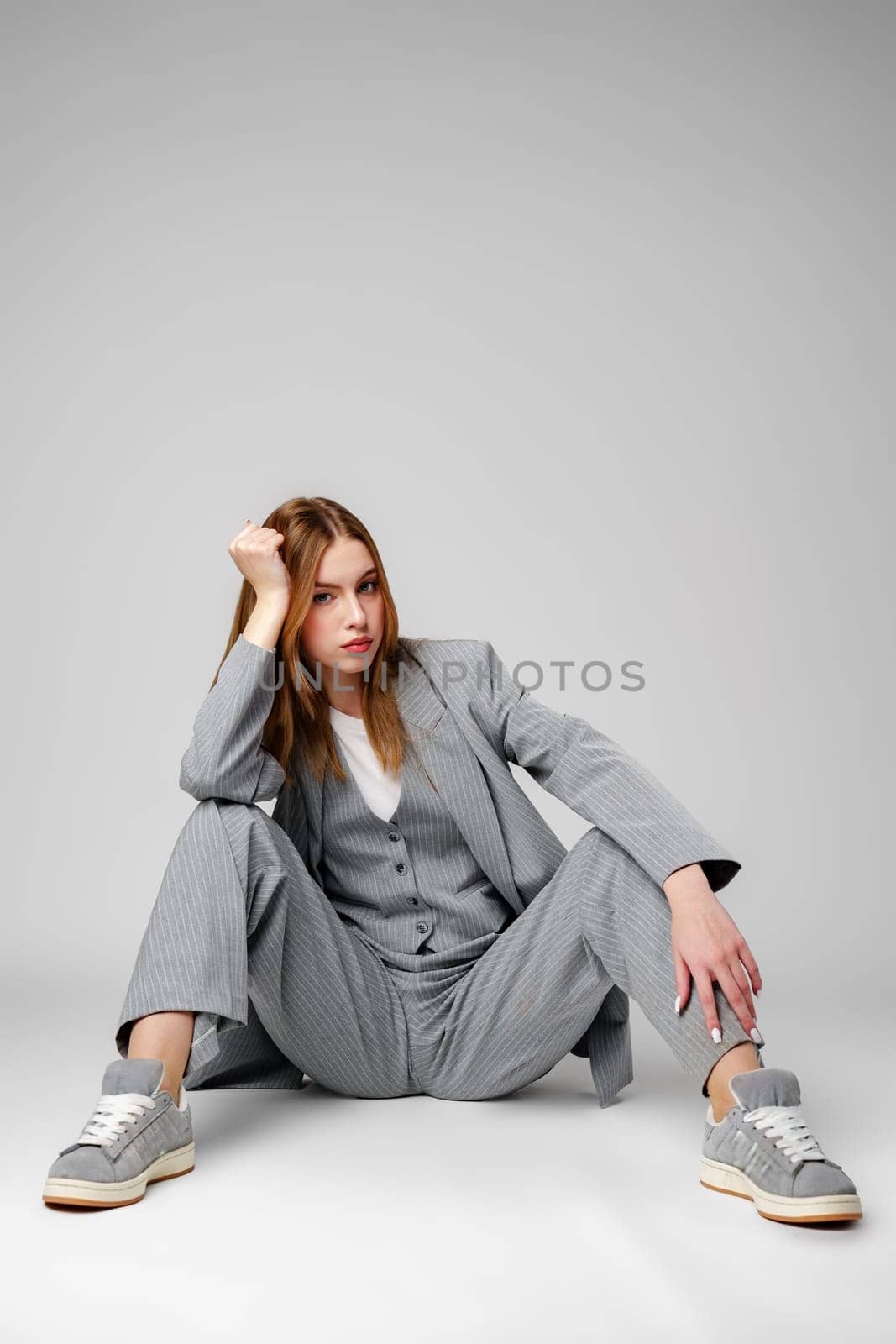 Young Woman in a Gray Suit Sitting on the Floor in Studio by Fabrikasimf