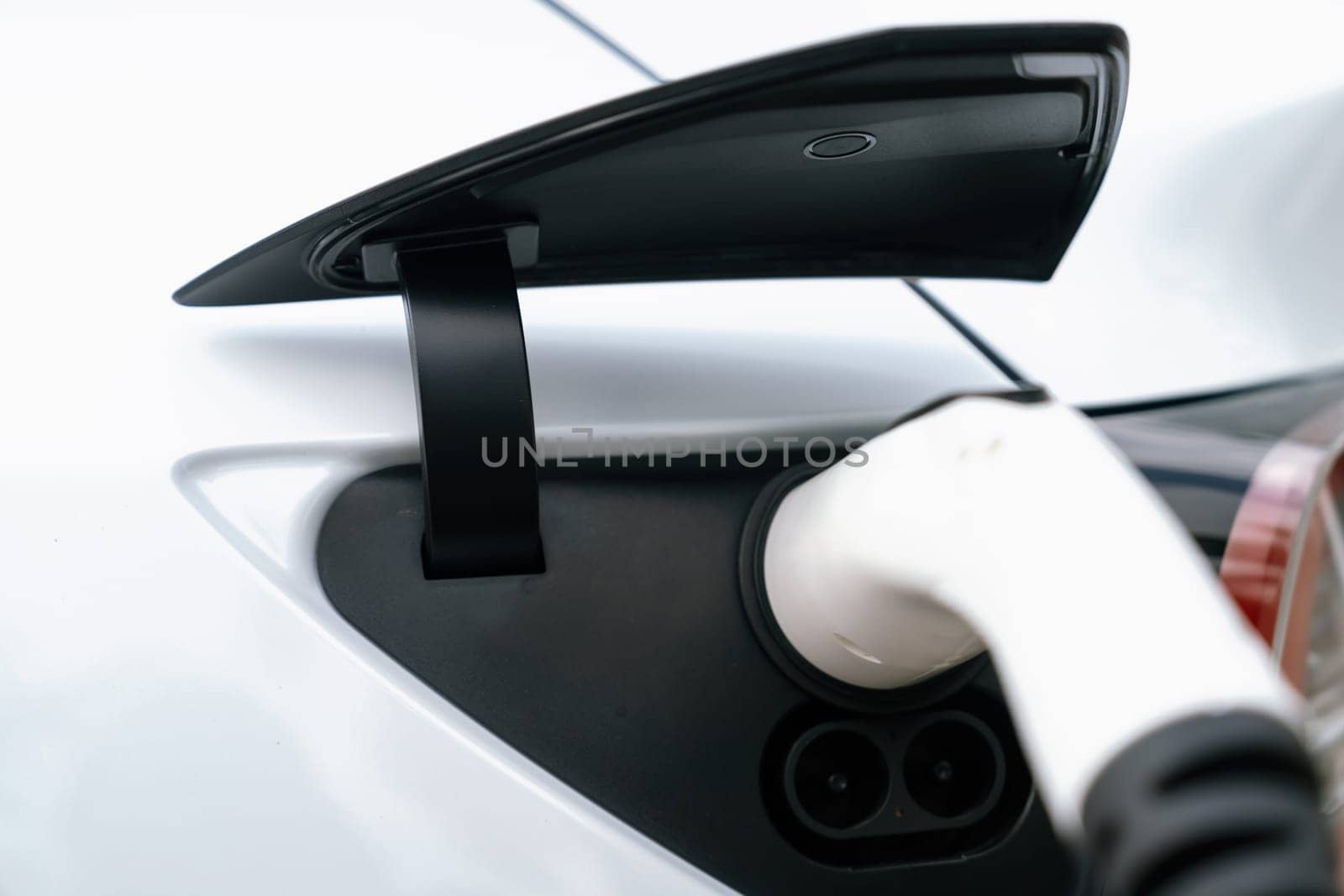 Closeup EV charger plug handle attached to electric vehicle port, recharging battery from charging station. Modern designed EV car and clean energy sustainability for better future concept. Synchronos