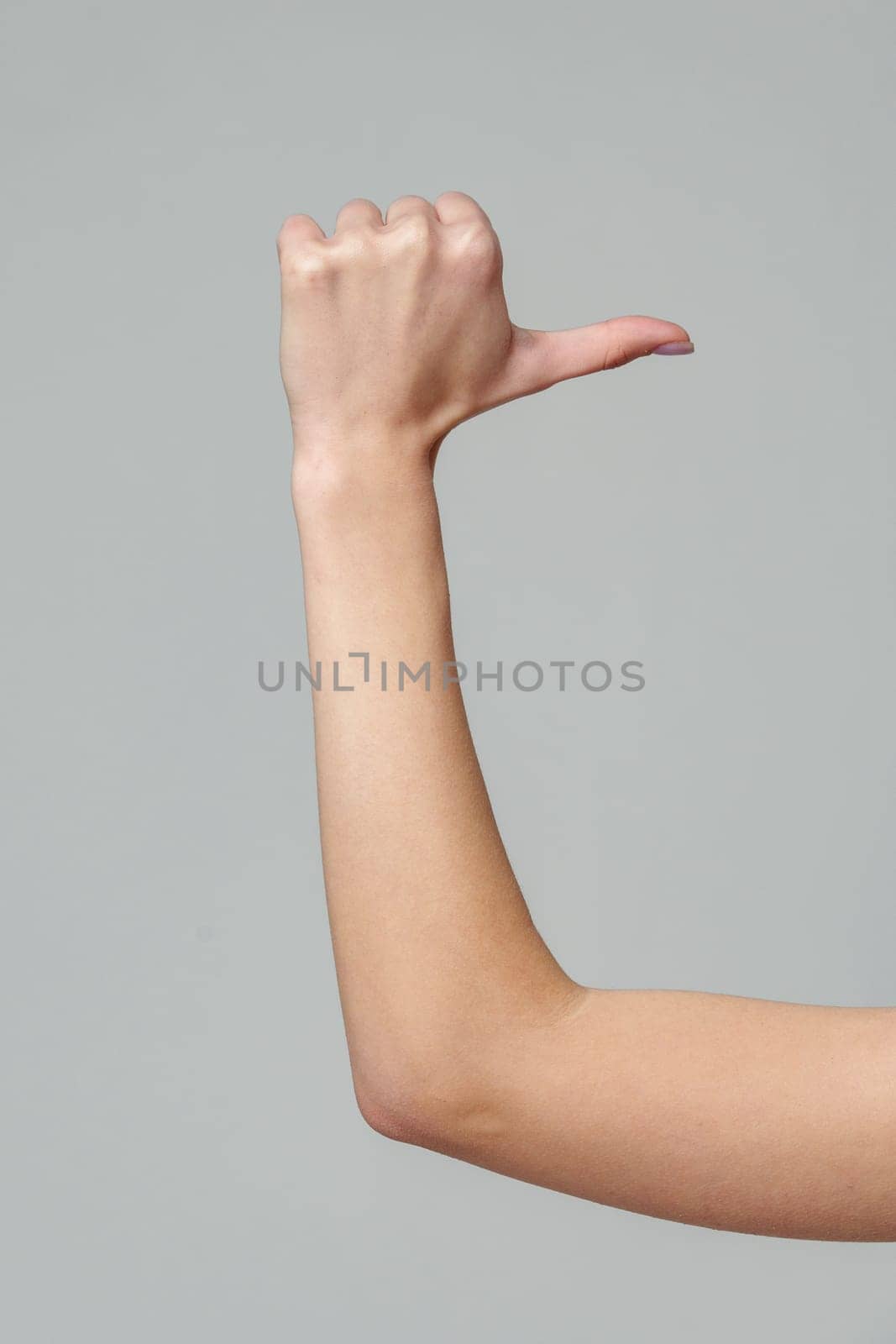 Female hand gesturing thumb up sign on gray background close up