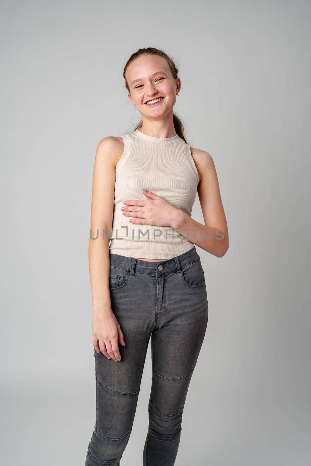 Girl in Beige Tank Top and Grey Jeans on gray background in studio